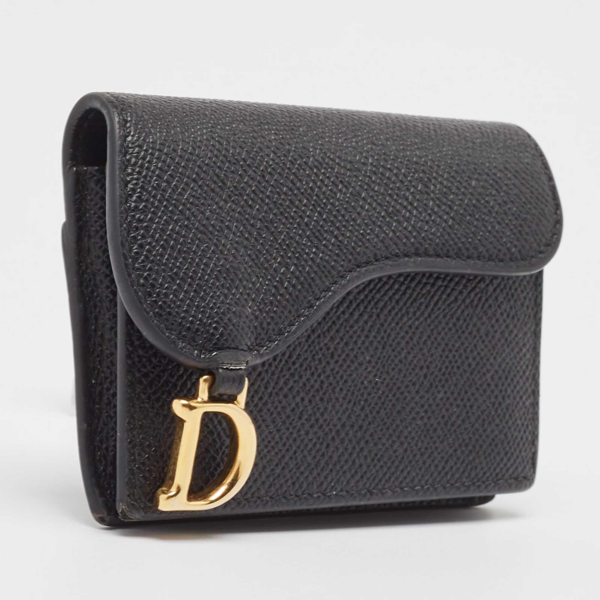 Das aus schwarzem Leder gefertigte Kartenetui von Dior ist mit mehreren Fächern ausgestattet, die durch eine Klappe gesichert werden, die von der kultigen Saddle-Tasche übernommen wurde. Abgerundet wird die Kreation durch den D-Charme auf der
