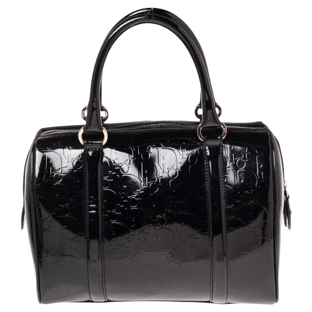 This Christian Dior Boston bag is crafted from black oblique monogram patent leather and detailed with silver-tone accents. Featuring zip closure, this bag comes with two rolled handles and stands on a sturdy base. The bag opens to reveal a spacious