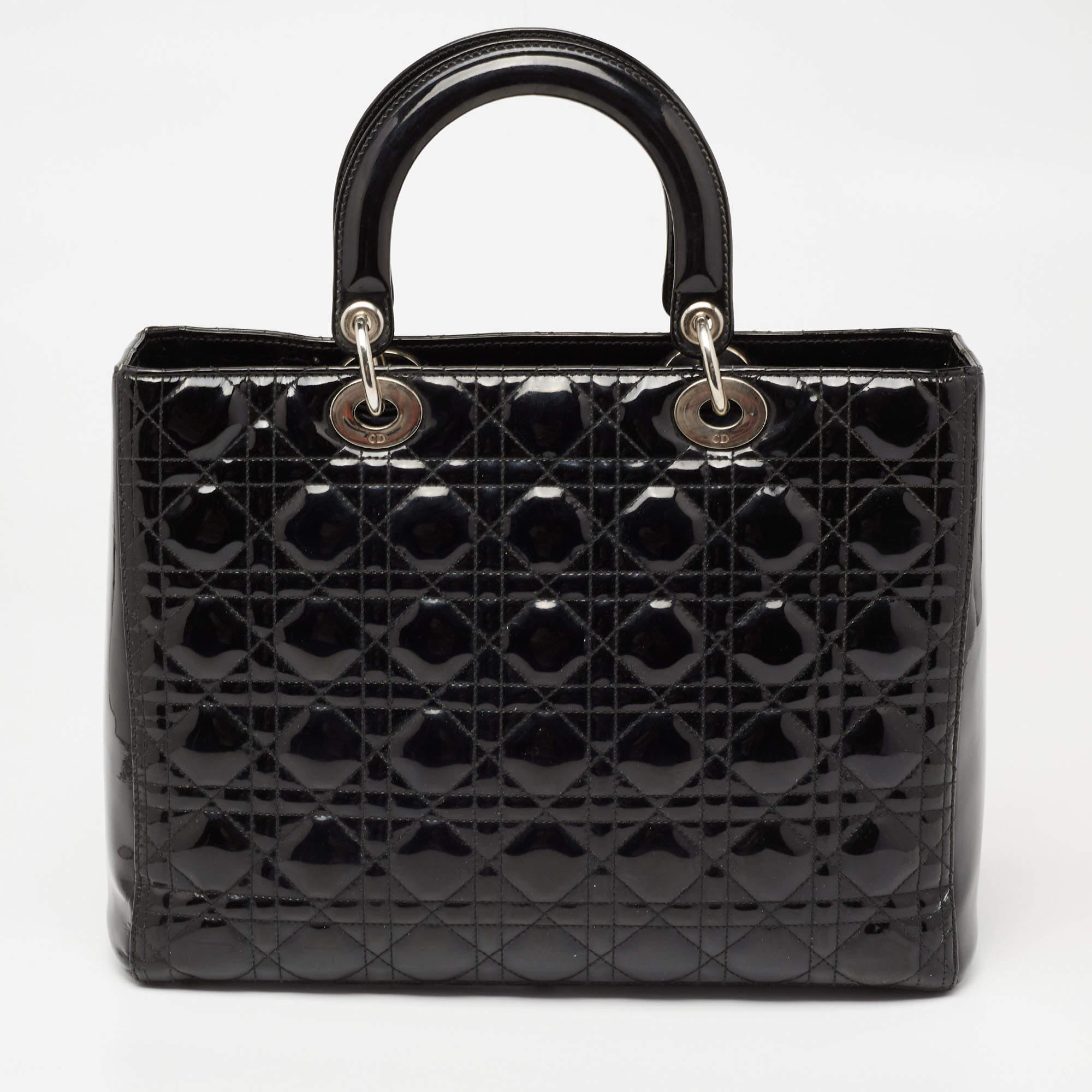 A timeless status and great design mark the Lady Dior tote. It is an iconic bag that people continue to invest in to this day. We have here this large Lady Dior tote crafted from black Cannage patent leather. The bag is complete with two top