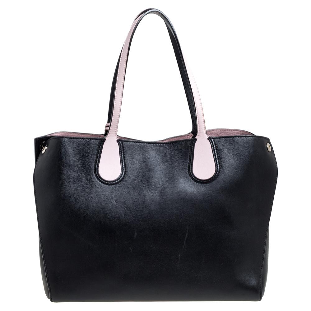 This Dior tote is a perfect companion for daily use. Crafted from supple leather in black with pink leather details, it is provided with silver-tone hardware. The bag features two flat handles, studs to secure its bottom, and pink-tone Dior charms.