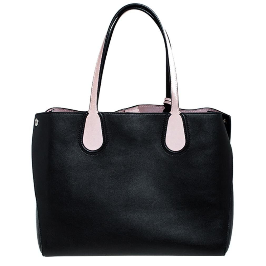 This Dior Addict tote is a perfect companion for daily use. Crafted from leather in black with pink leather details, it is enhanced with silver-tone hardware. The bag features two flat handles, studs to secure its bottom, and pink-tone Dior charms.