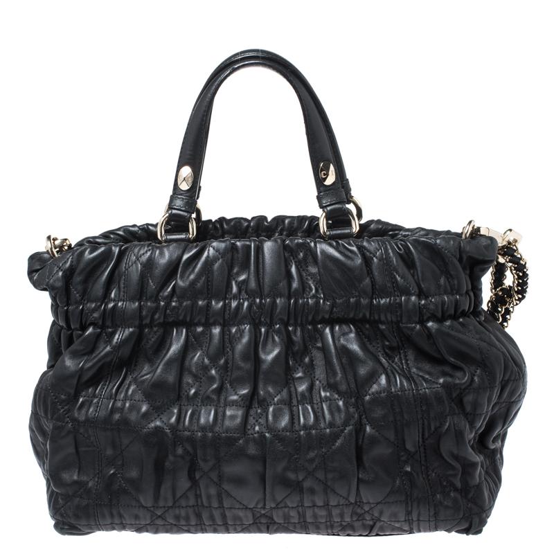 This chic bag from Dior is crafted from leather and features a Cannage quilted exterior. The black tote comes with dual handles and a leather-chain strap. The buttoned closure opens to a matching leather-lined interior that has