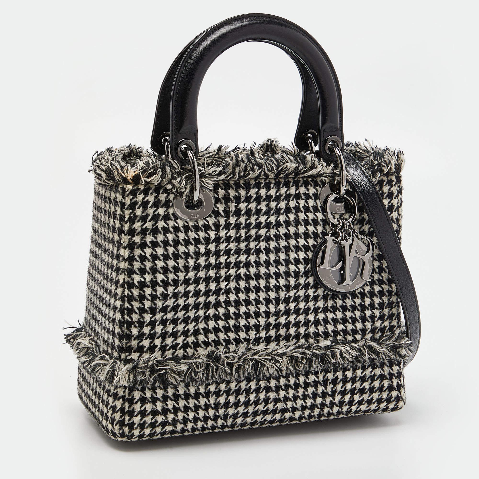 The Lady Dior tote is a creation that has gained recognition worldwide, continuing a legacy of being a coveted bag. This black & white tote has been crafted from tweed fabric and it carries a houndstooth pattern. It is equipped with a leather