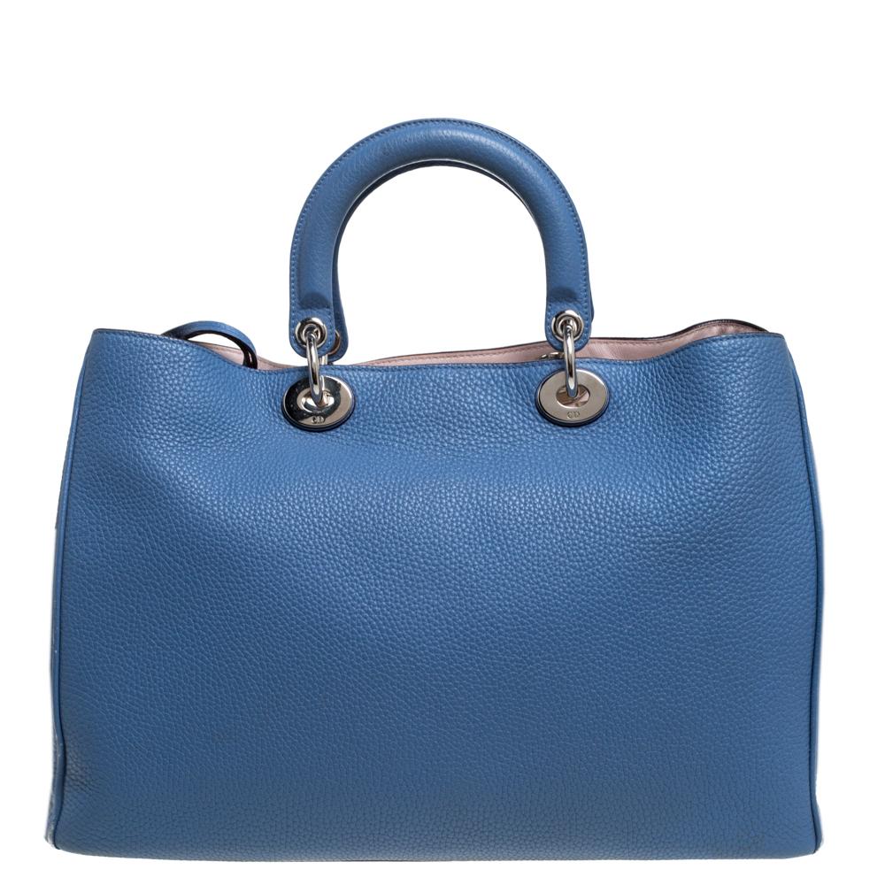 The Diorissimo tote from Dior is a piece that has never gone out of style. The leather bag comes in a blue shade with silver-tone hardware and Dior letter charms. It features double top handles and protective feet at the bottom. A snap button