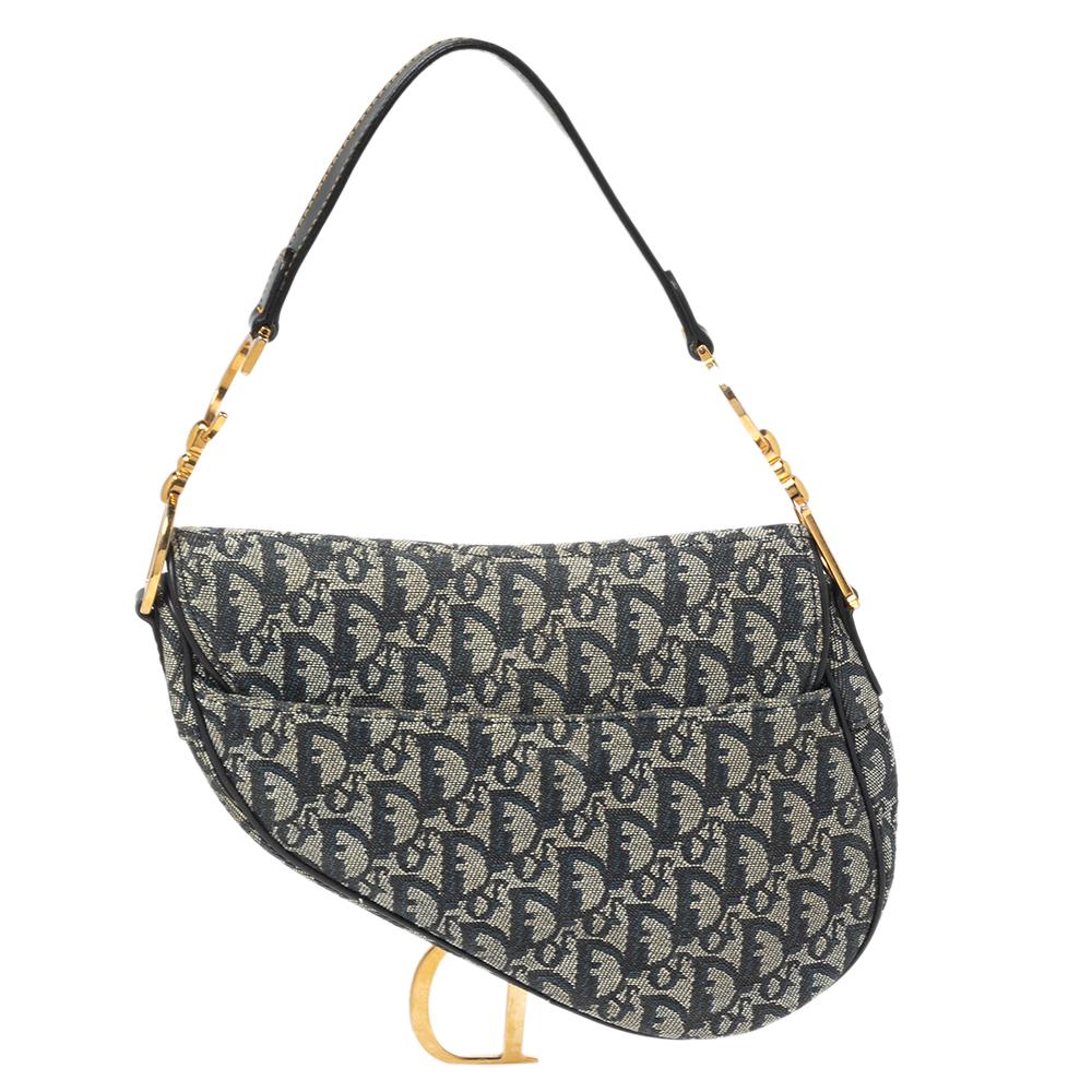 This Saddle bag is an iconic style designed by the House of Dior. It flaunts an emblematic Dior Oblique pattern on the blue denim exterior with contrasting gold-toned accents that give this piece a timeless appearance.