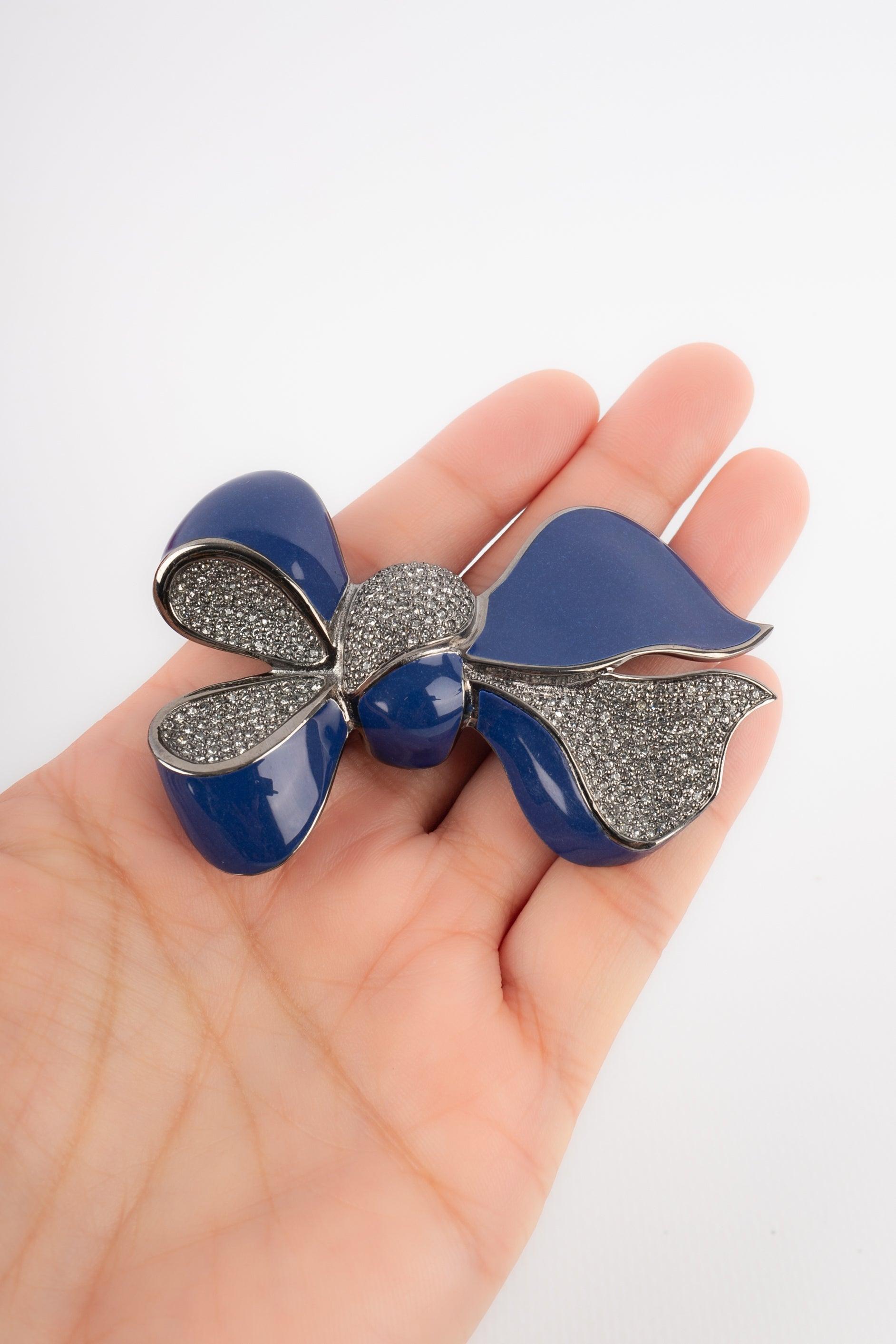 Dior - Dark-silvery metal brooch representing a bow enameled with blue and rhinestones. Jewelry from the 2000s.

Additional information:
Condition: Very good condition
Dimensions: 6.5 cm x 4.5 cm

Seller Reference: BR103