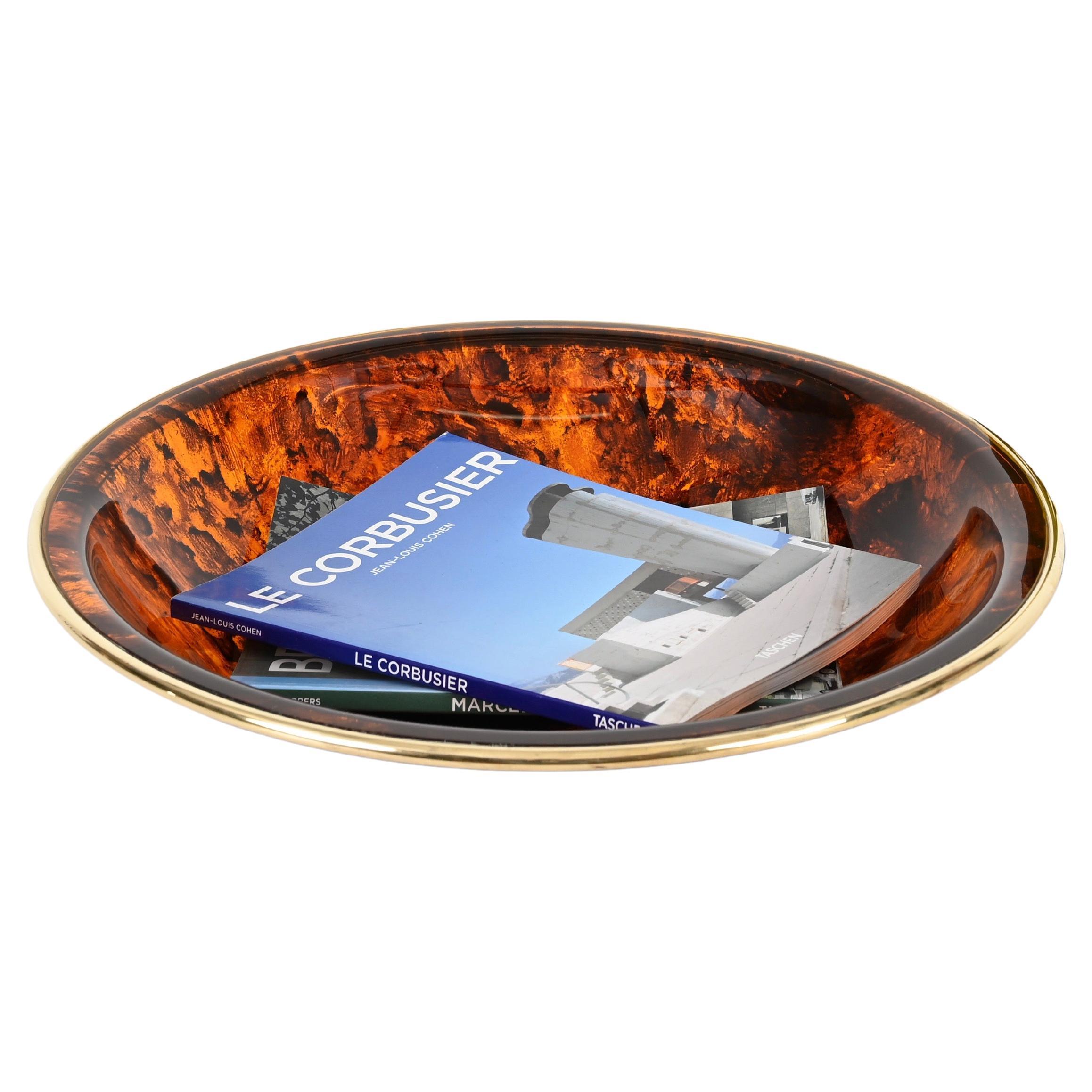 Marvelous mid-century decorative round bowl, centerpiece or magazine rack in a stunning tortoiseshell effect lucite with a brass rim. This stylish object was produced in Italy during the 1970s and its design is attributed to a Dior Home