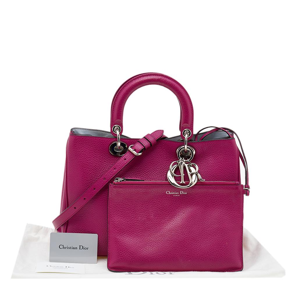 The Diorissimo shopper tote is a timeless beauty. The Dior leather bag comes in a bright pink shade with silver-tone hardware and Dior letter charms. It features double top handles and protective feet at the bottom. A snap button closure opens to