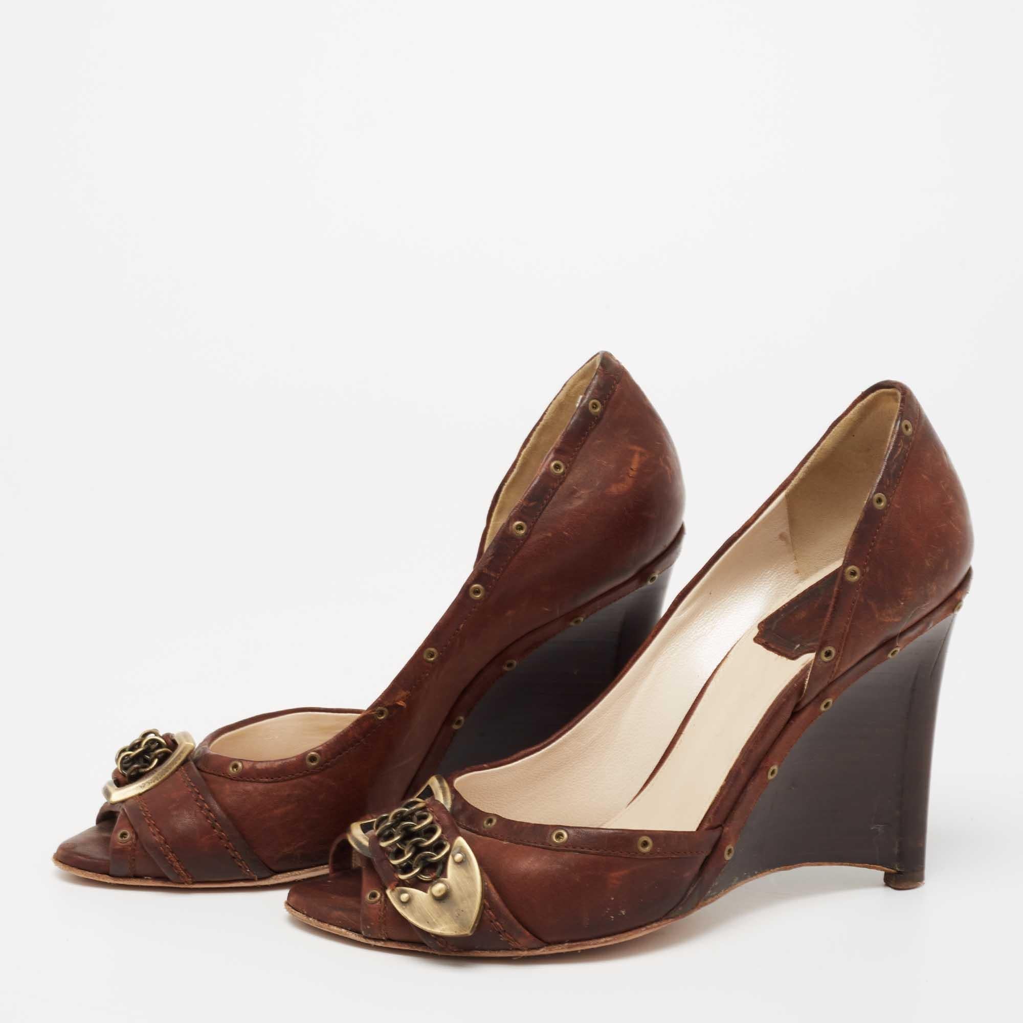 Exhibiting a chic silhouette enhanced with excellence these pumps from the House of Dior exude signatory style They are designed using brown leather on the exterior. These pumps have wedge heels peep toes and a slip on feature. Look great as you