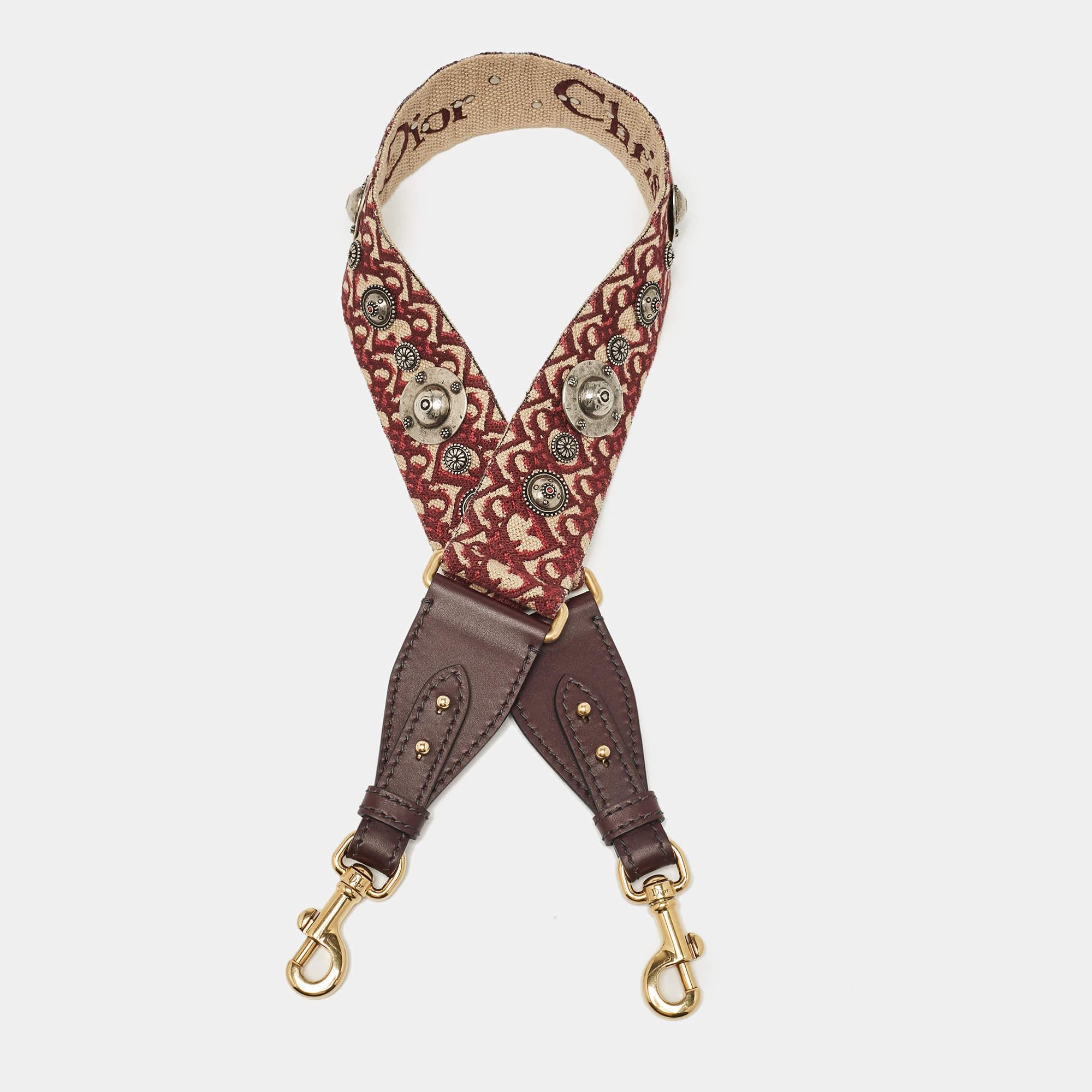 Dior te trae esta bandolera súper chic que podrás lucir con tu colección de bolsos. A la correa de lona se le añaden detalles de tachuelas y adornos de piel. Se completa con dos cierres metálicos.