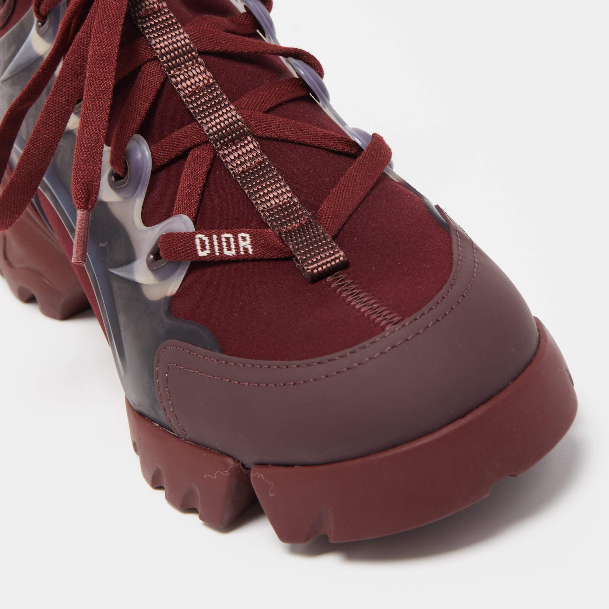 The Dior D-Connect sneakers are a stylish footwear choice. These sneakers feature a blend of burgundy PVC and fabric materials, providing durability and a unique aesthetic. With the iconic chunky shape, they offer a fashionable and comfortable