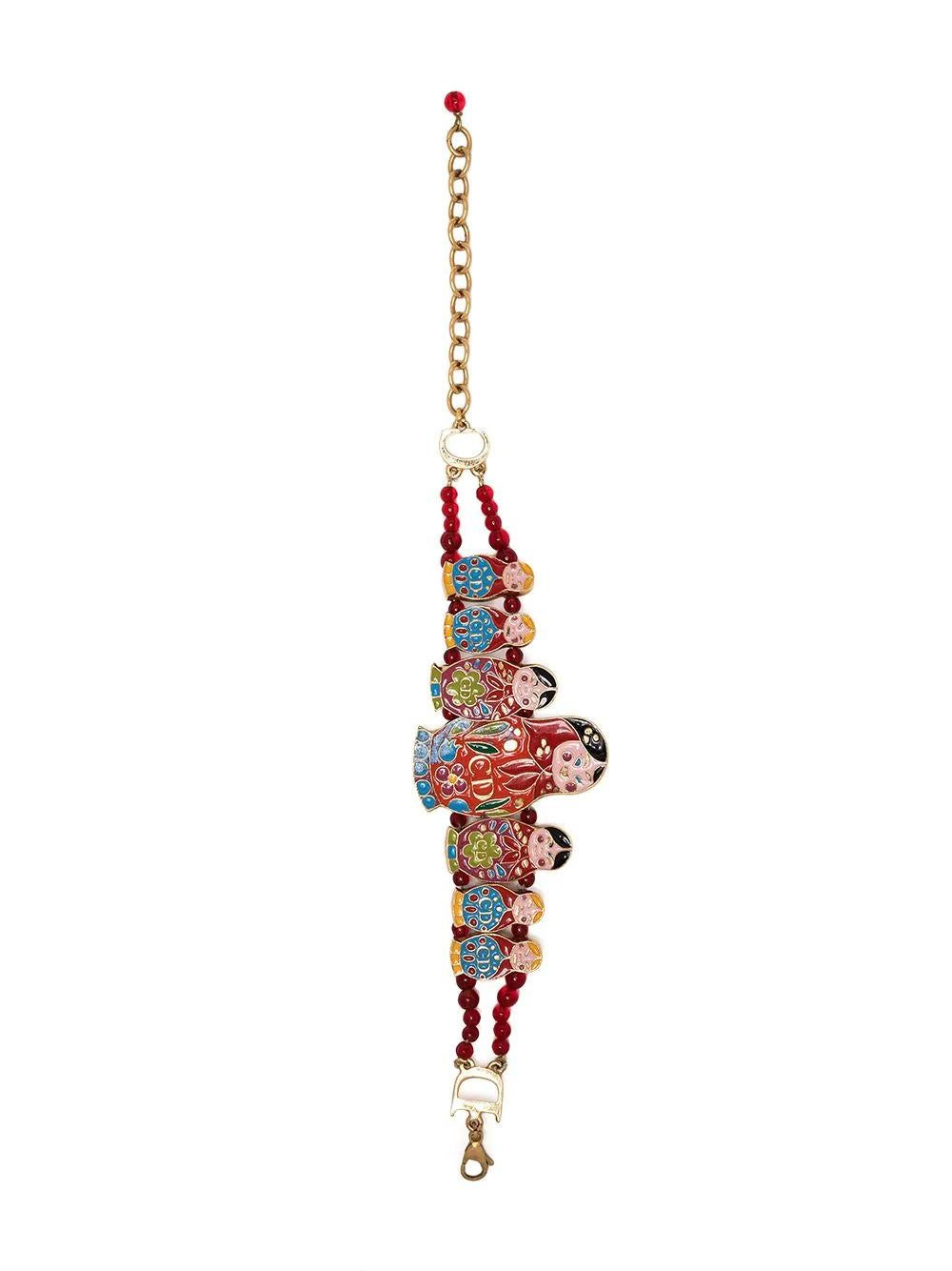 Con siete muñecas rusas policromadas marcadas con CD que descansan sobre una cadena doble adornada con cuentas grises y rojas, esta pulsera vintage de segunda mano de los años 90 Dior by John Galliano se inspira en las muñecas rusas Matryoshka. En