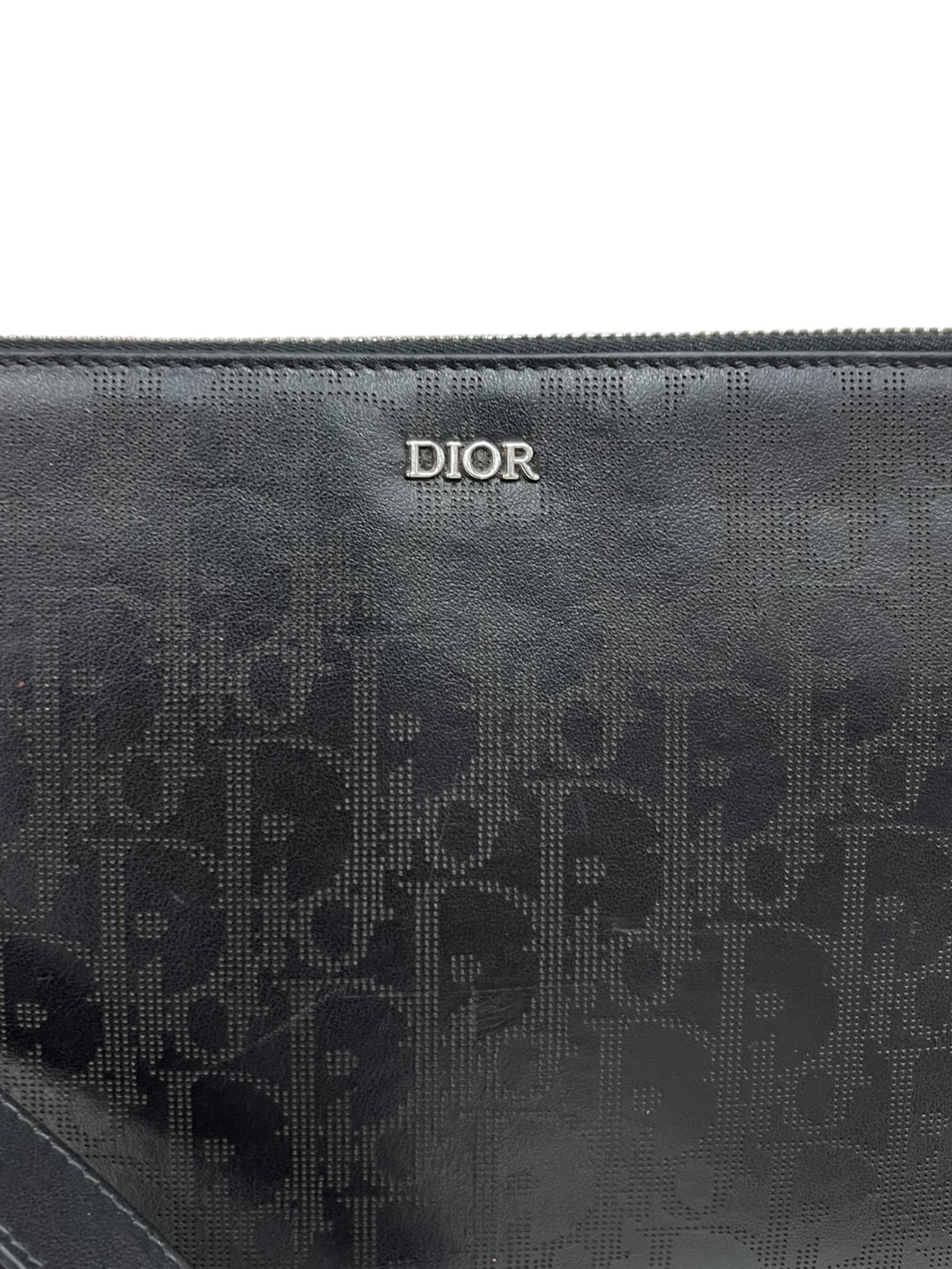 Clutch firmata Dior, modello Man, realizzata in pelle oblique galaxy con hardware argentati. Dotata di una chiusura superiore con zip, internamente rivestita in tessuto nero, capiente per l’essenziale. Munita di polsino rimovibile, l’articolo si