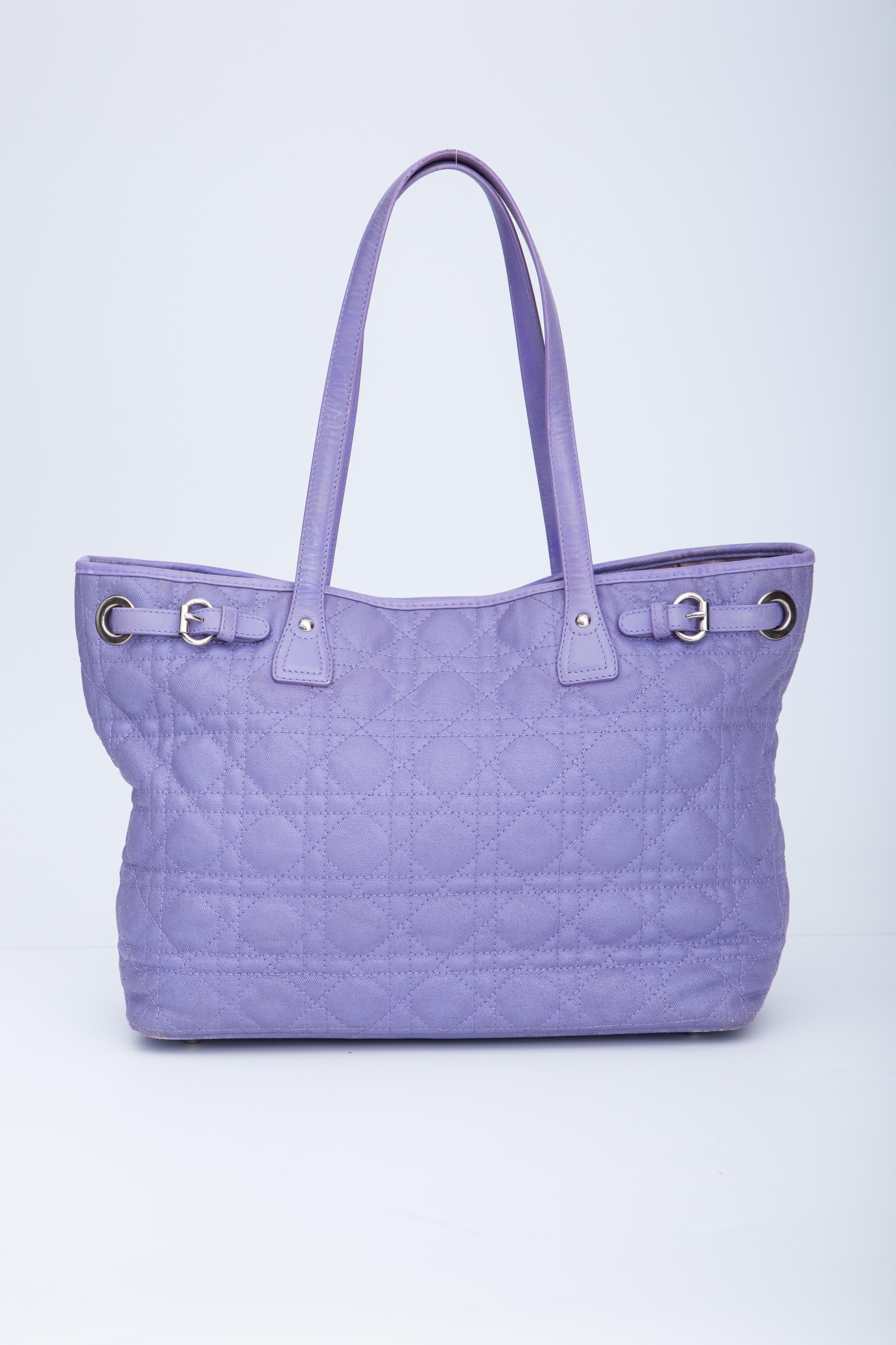 This tote is made of geometric quilted coated canvas in purple. The bag features dual flat leather strap top handles, polished silver hardware including a Dior hanging charm, an open top with snap closure and a purple fabric interior with a zipper