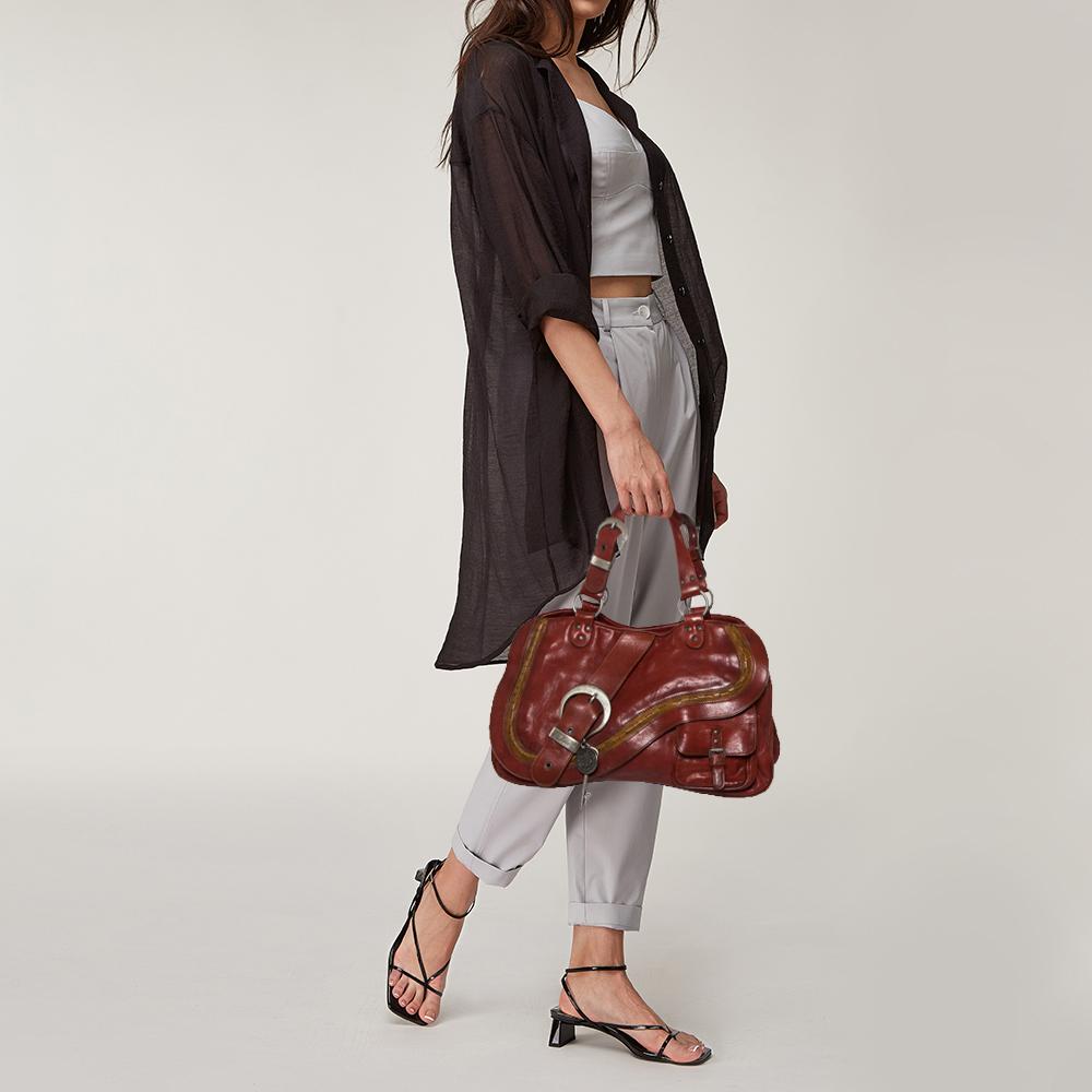 From the house of Dior comes this Double Saddle bag which is an excellent blend of elegance and style. It comes in a beautiful copper brown hue, perfect for making a statement. The bag features a chunky buckle as well as a key on the front and a