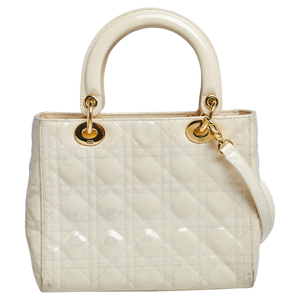 A timeless status and great design mark the Lady Dior tote. It is an iconic bag that people continue to invest in to this day. We have here this beauty crafted from cream patent leather. The bag has a spacious fabric-lined interior housing a zipper