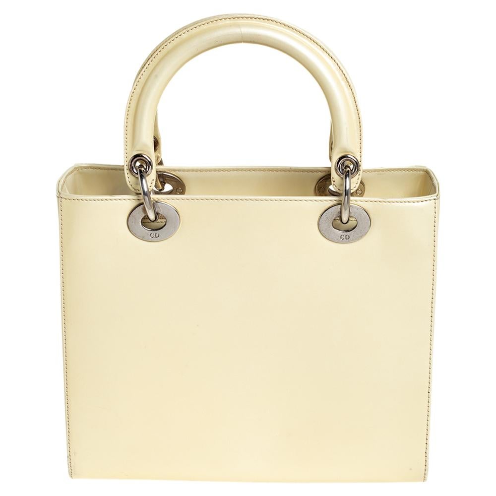 The Lady Dior tote from Dior is a timeless piece. The leather bag comes in a luxurious shade of cream with silver-tone hardware and 'Dior' letter charms. It features dual top handles, a detachable shoulder strap, and protective studs at the bottom.