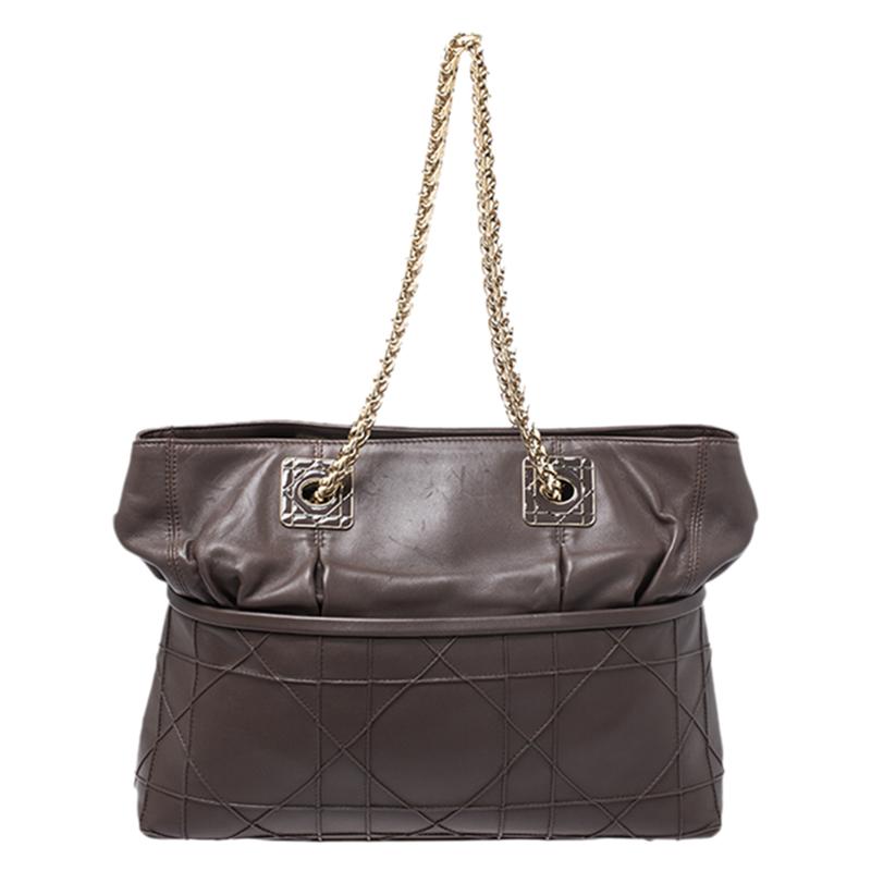 This chic and feminine tote is from Dior. The bag is crafted from Cannage-detailed leather. Dark brown in color, the tote is easy to carry around. The bag features two chain straps, protective metal feet and a top snap closure that opens to a