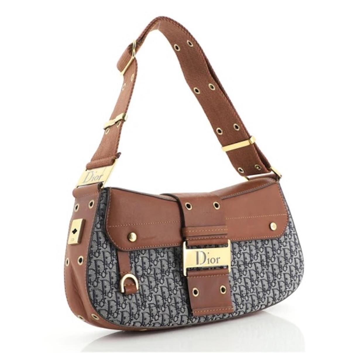 This Dior bag from the 2002 street chic collection, designed by John Galliano, is crafted in navy canvas with jacquard diorissimo monogram stitch. It features a structured shape, cowhide leather flap, and a belt with snap closure. Metallic logo
