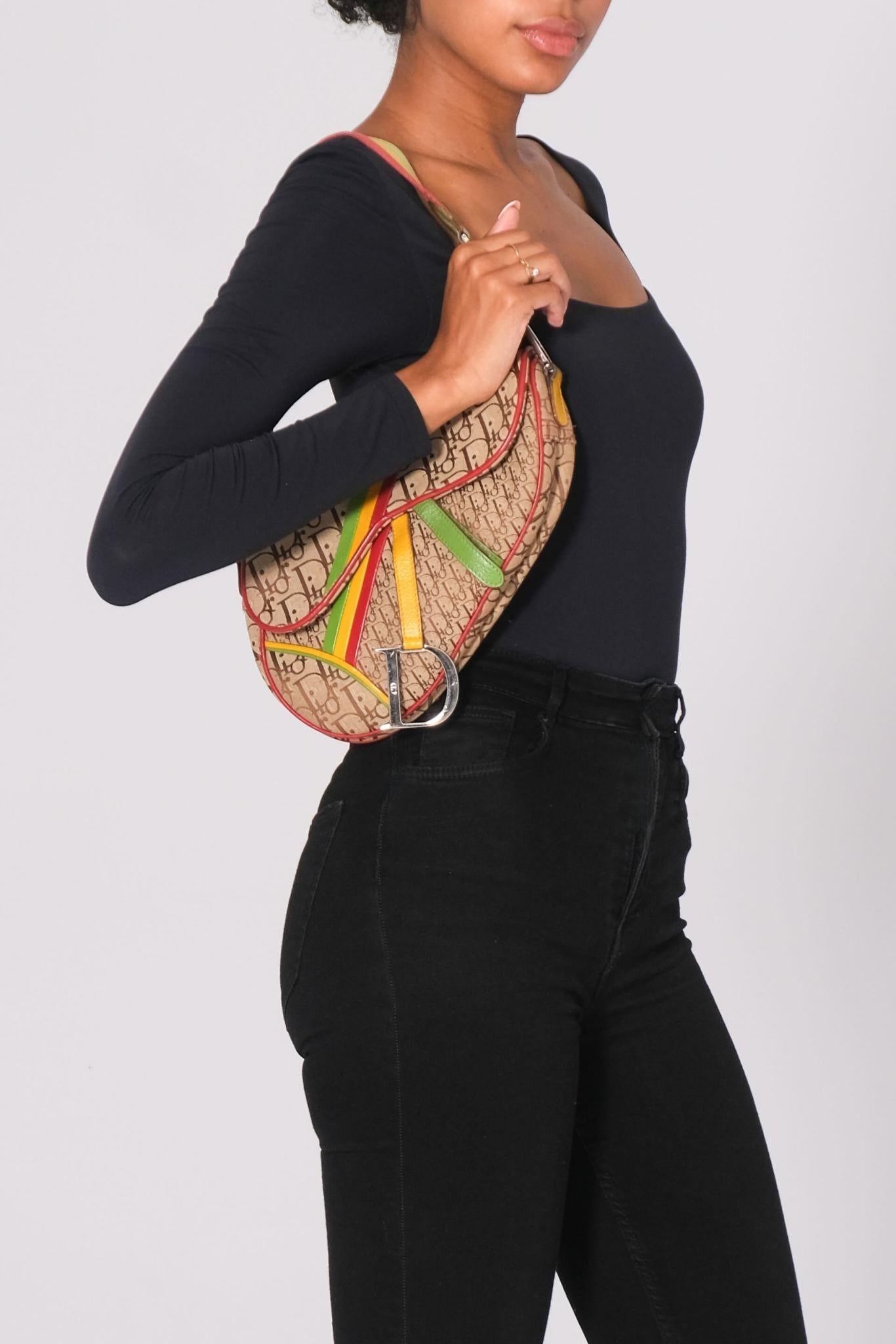 This vintage Dior saddle bag is made of brown canvas with a diorissimo monogram print with Rasta details. The bag features leather trim, a flat leather shoulder strap, a front flap with velcro closure and a back slip pocket. The interior is finished