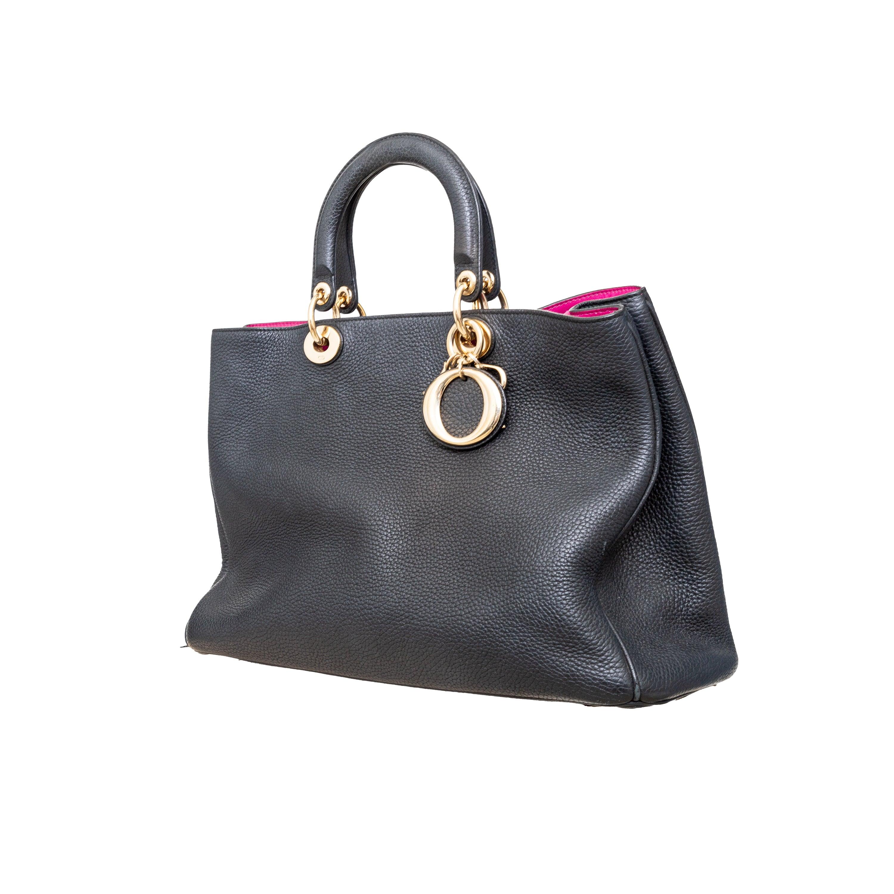 The Dior Diorissimo Tote Bag features a black calfskin grained leather design with signature Dior charms and gold tone hardware. The top snap button closure and removable shoulder/crossbody strap make it practical, while the pink leather lining with