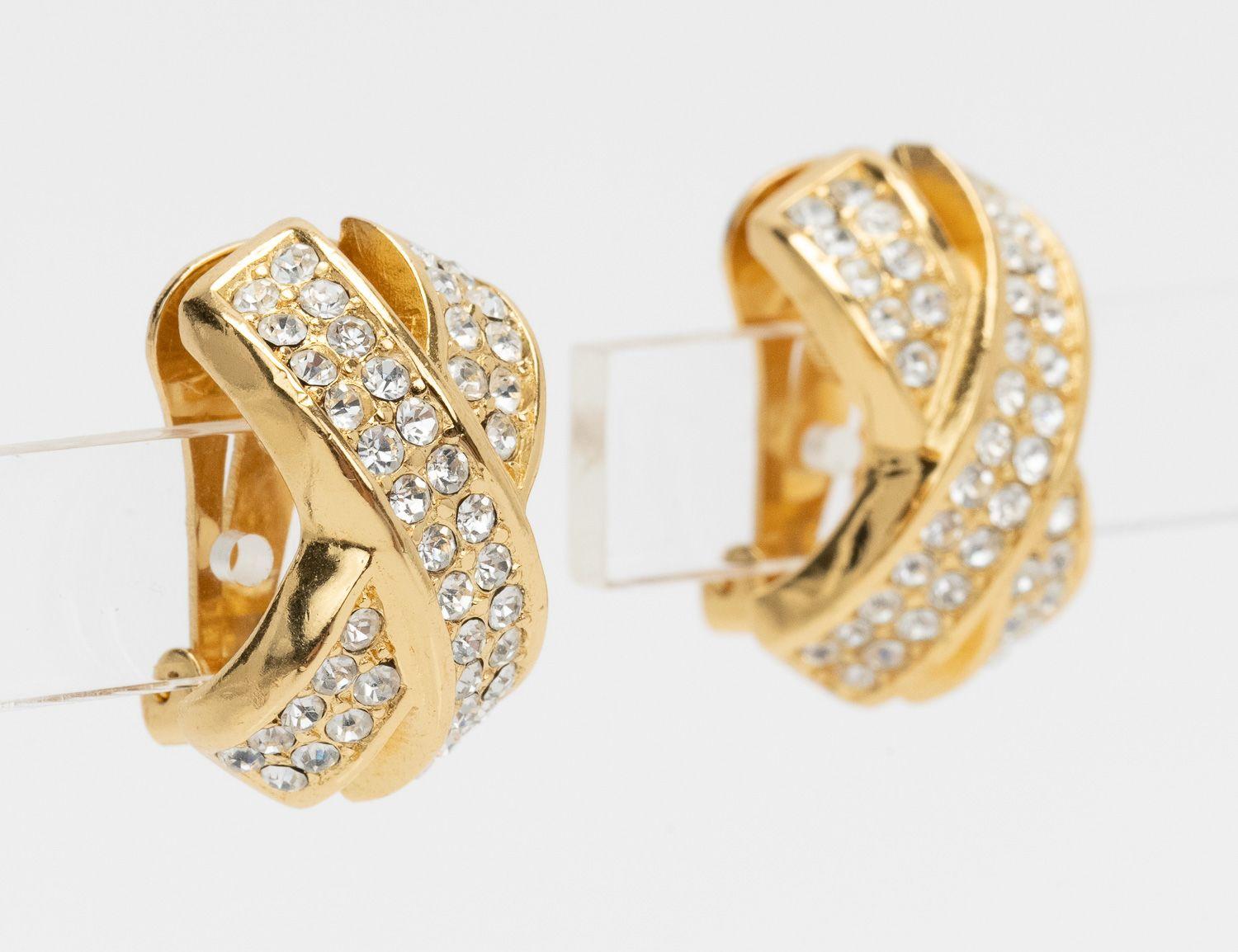 Orecchini Christian Dior a forma di fasce incrociate in metallo dorato con strass. In ottime condizioni.