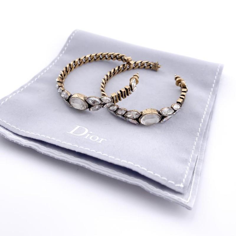 The earrings are from Maison DIOR. They are hoop earrings in aged gold metal, set with rhinestones. The DIOR mark is displayed on each of the loops. At the end of each hoop is the little star DIOR.
The pair of earrings is in a very good condition.