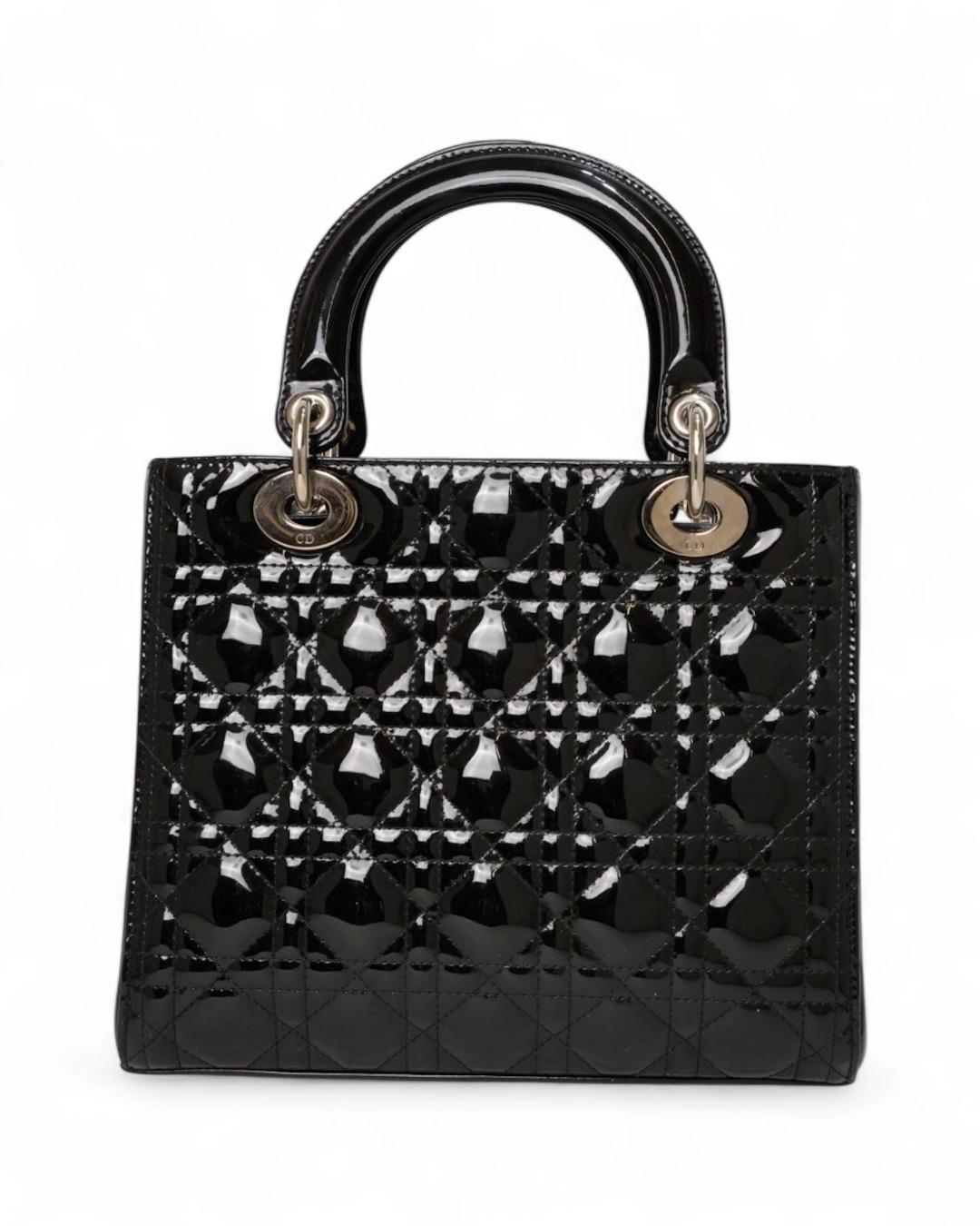 Borsa firmata Dior, modello Lady nella misura medium, realizzata in pelle lucida nera con motivo cannage e hardware dorato. Dotata di una chiusura superiore a zip, internamente rivestita in tessuto logato tono su tono con comoda tasca, la borsa è