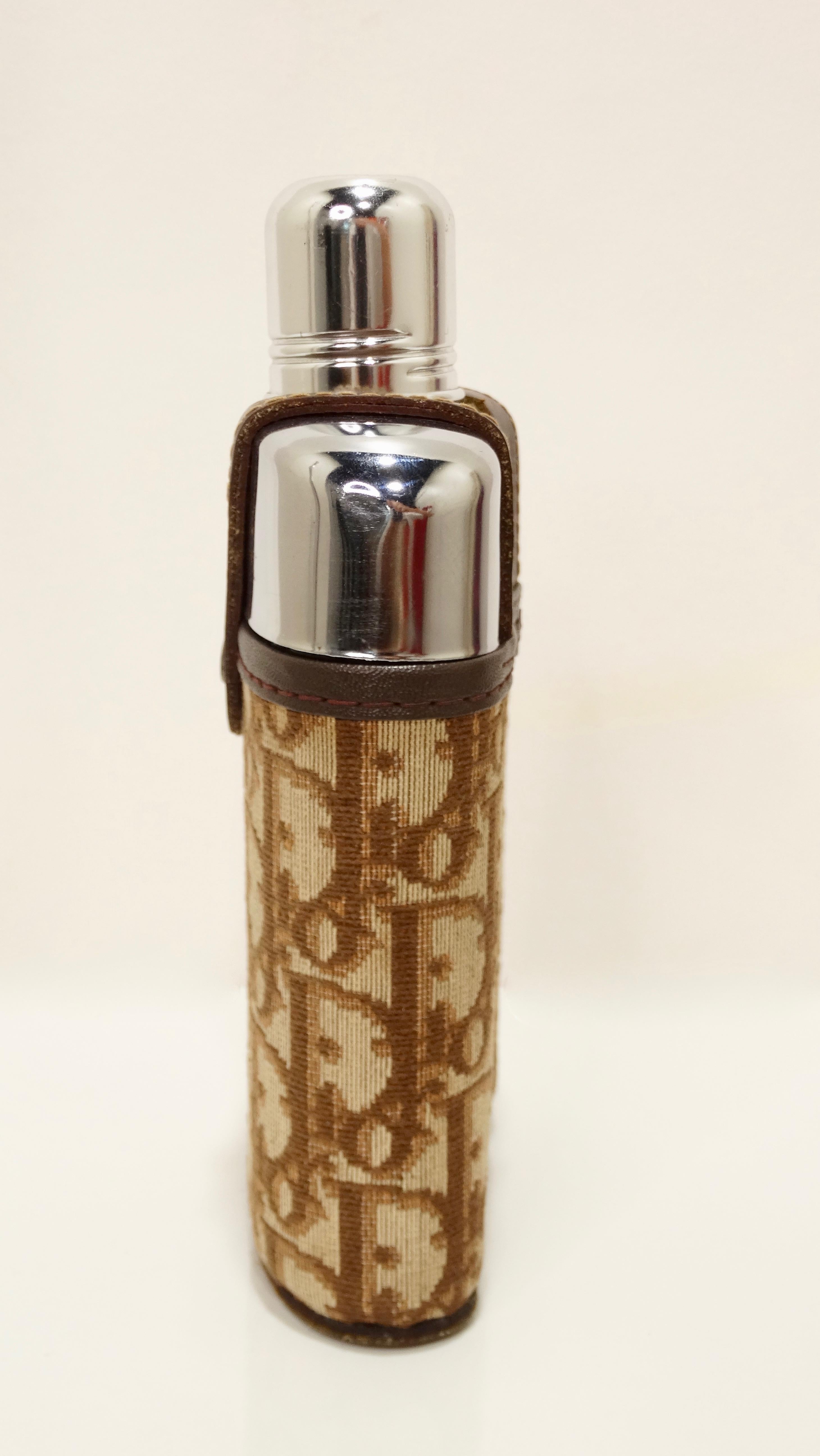 Sip in style with this rare Dior flask! Circa late 20th century, this flask features a thick glass bottom and stainless steel top with a removable Dior brown/tan monogram jacket case. Jacket case includes a leather trim and snap button closure.