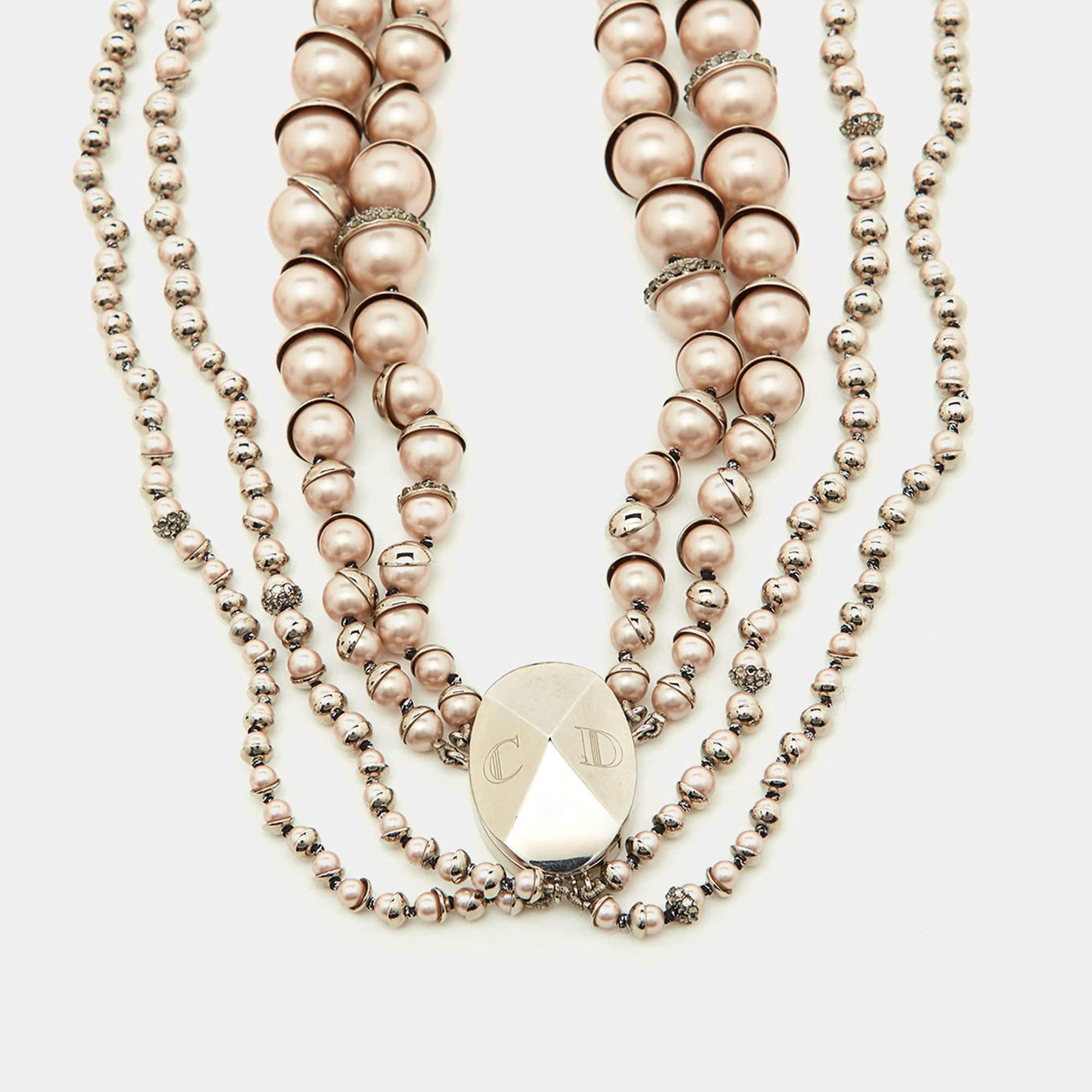 The Dior Mise En Dior necklace is an exquisite piece of jewelry. It features a multi-strand design with pink faux pearls and sparkling crystals, set in a silver-tone metal. This luxurious necklace exudes elegance, sophistication, and timeless