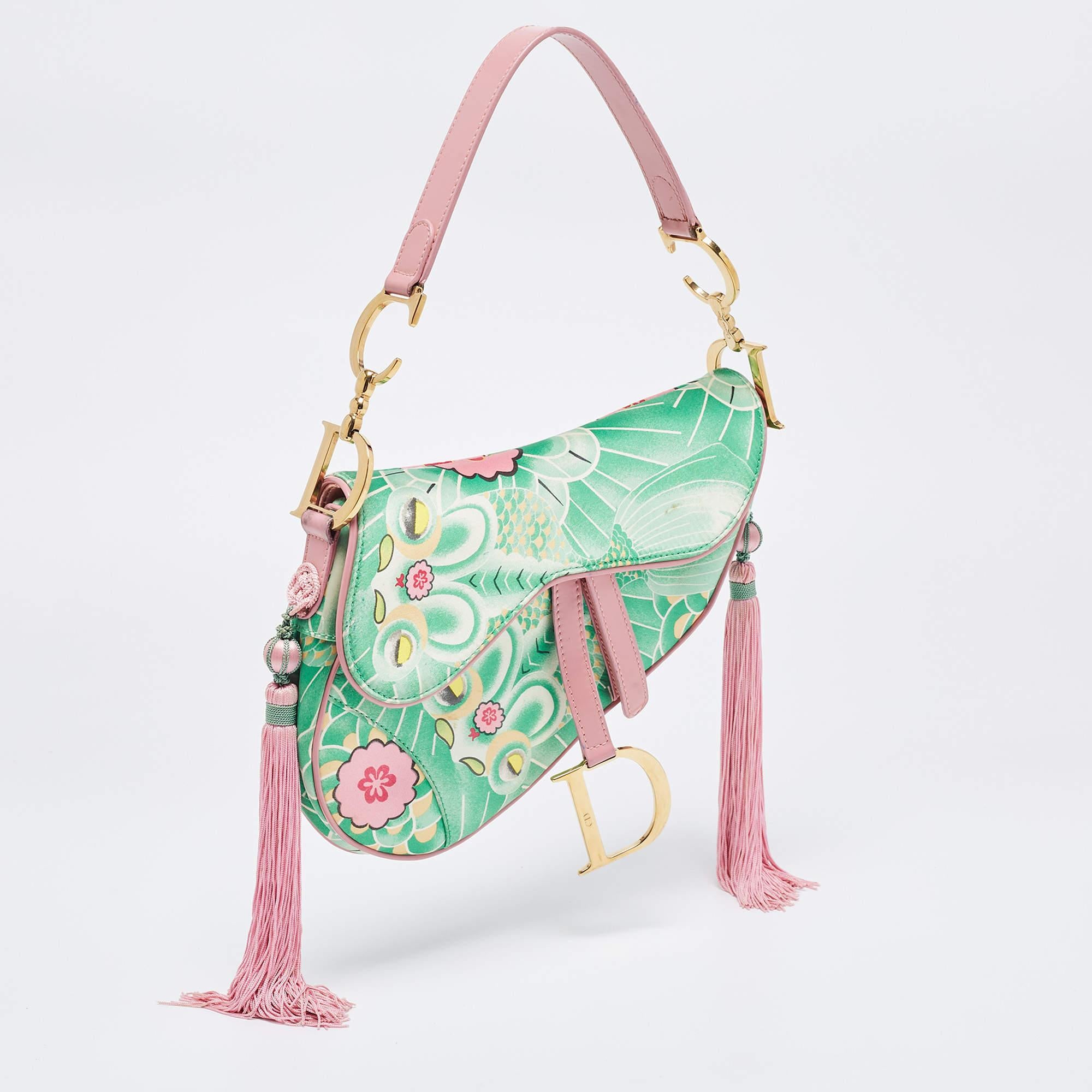 Designed by John Galliano, the Dior Saddle bag is an investment-worthy creation and an icon in the world of handbags. Here, we have a limited edition version of the bag called the 'Koi Saddle'. It is made from printed satin and detailed with pink