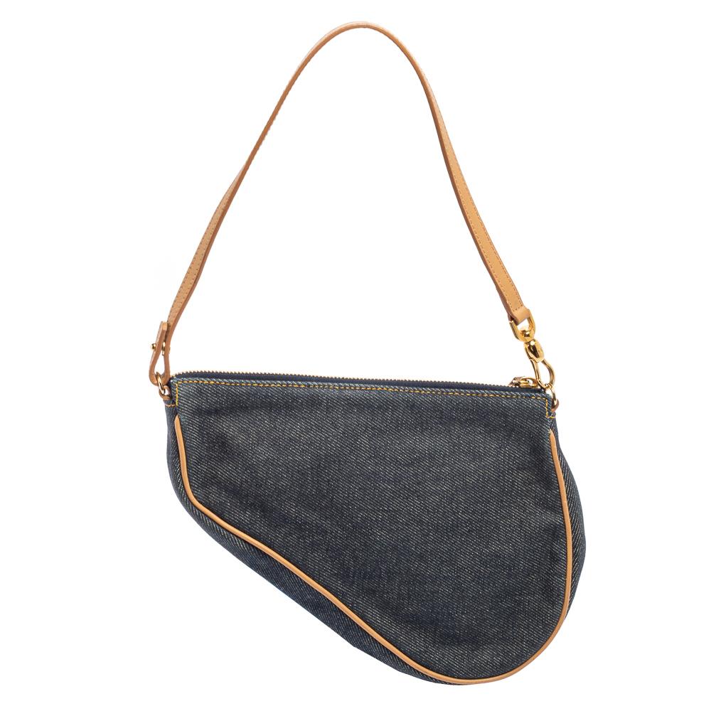 Owing to its uniquely-crafted silhouette and timeless elegance, the Saddle pochette bag from Dior remains one of the most sought-after designs of the brand. This version is carved using navy-blue denim. The Saddle pochette is complete with a