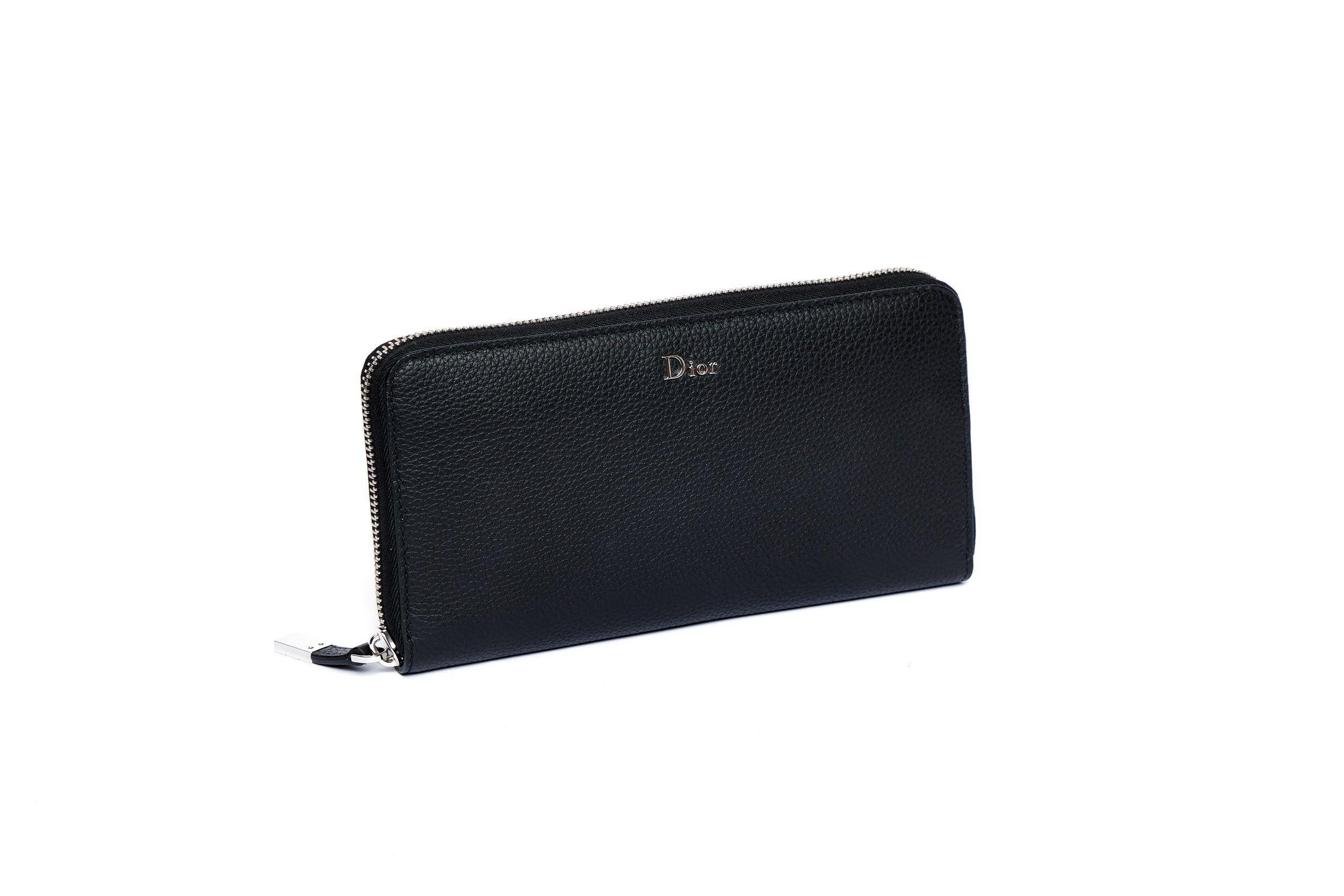 Black leather Dior wallet with a zip closure and silver metal hardware. In the inside are multiple card slots and compartments and a central zip compartment. The interior is also crafted of leather. The wallet is in excellent condition and comes
