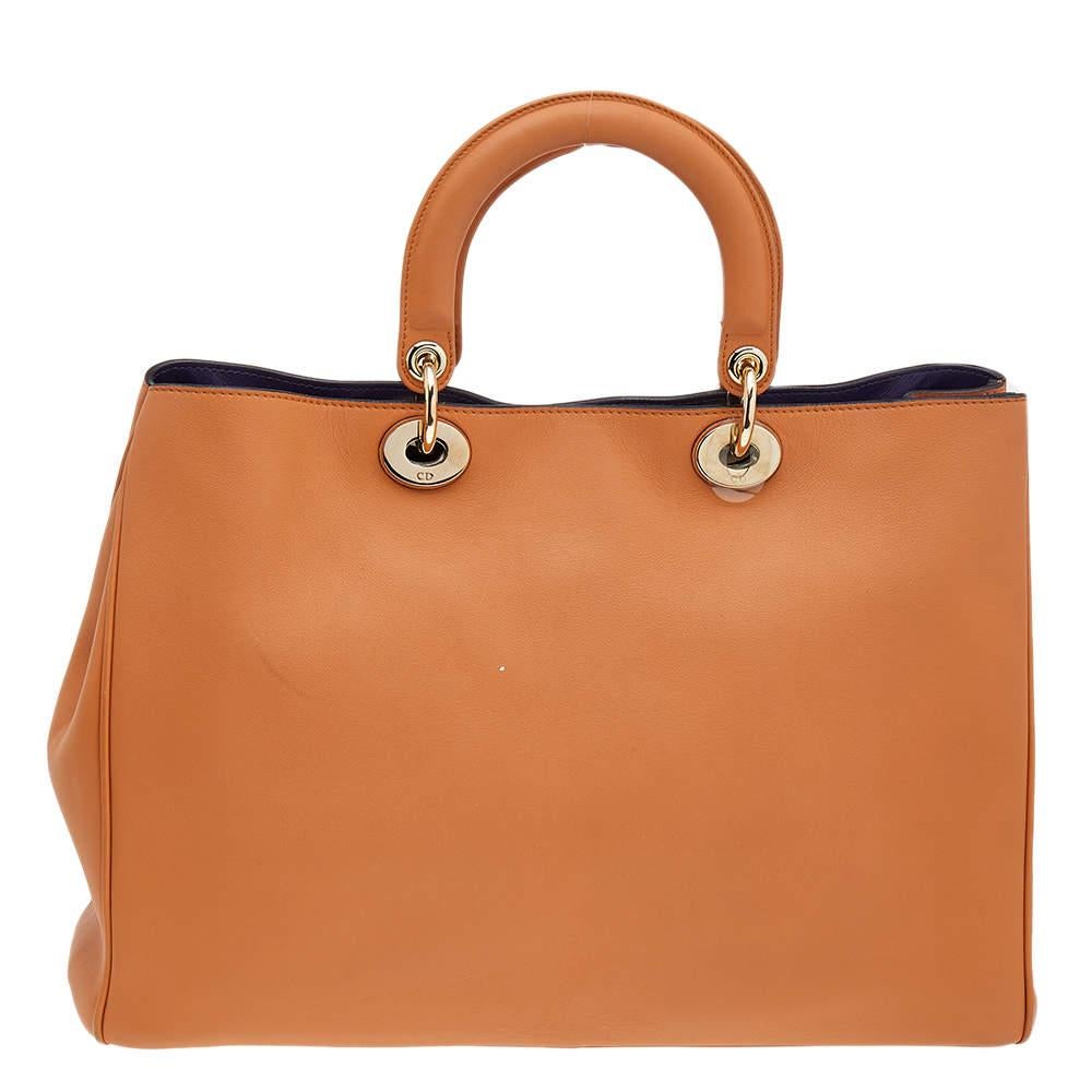 This Diorissimo Shopper tote from the House of Dior will help you keep your belongings safely and stylishly. It is made using orange leather on the exterior and is highlighted with gold-toned D.I.O.R charms on the front. It features dual handles, a