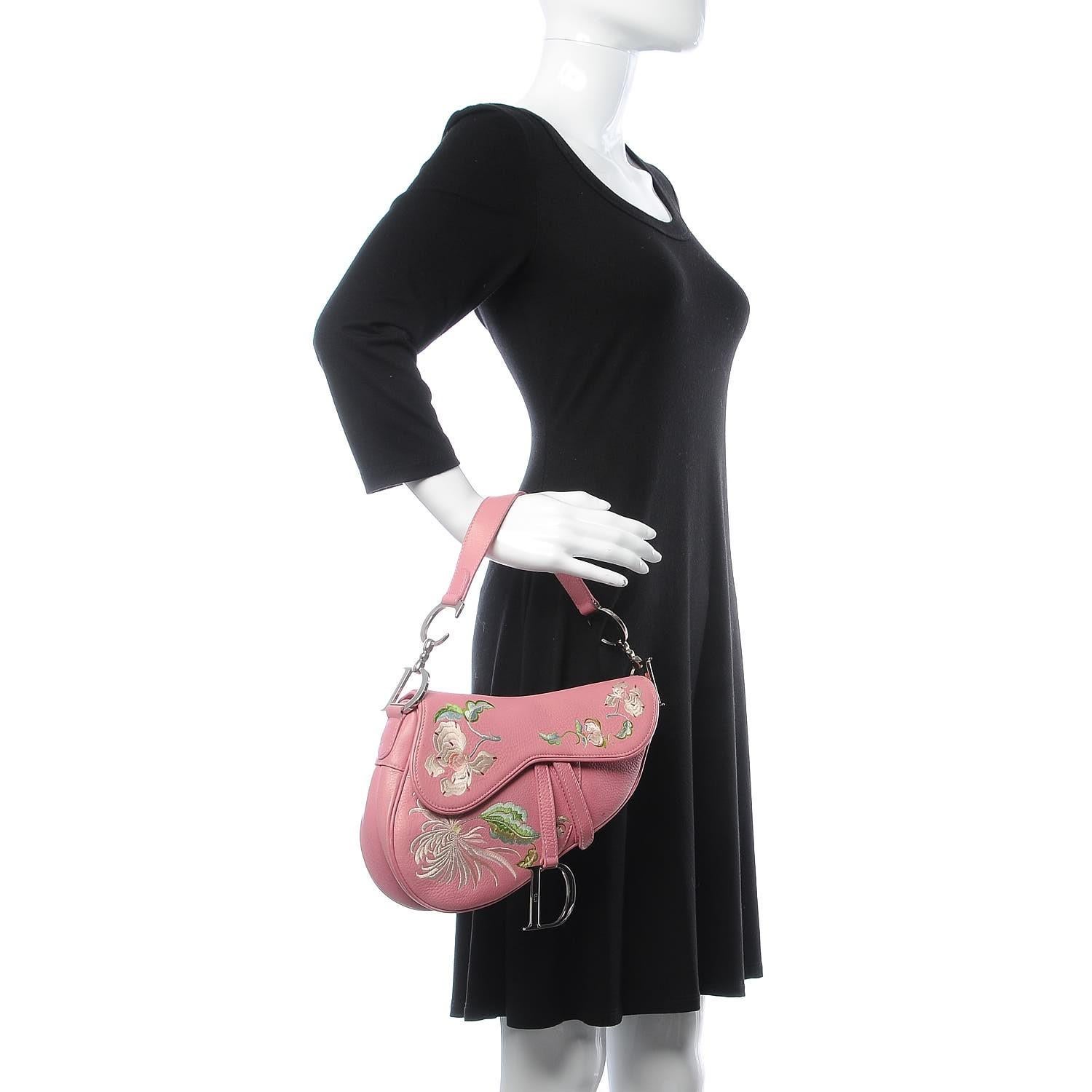 This Limited Edition saddle bag is made of luxurious pink leather flower embroidery. The bag features a looping leather shoulder strap with polished silver hardware and an embroidered floral decoration on the frontal flap. The frontal flap opens to