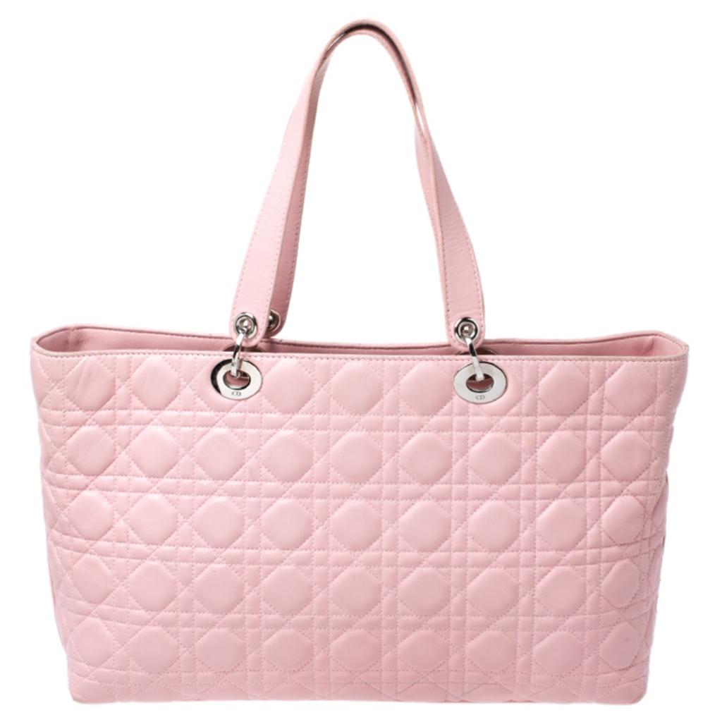 This Dior tote is exceptionally charming. The pink leather accented with the signature cannage pattern makes it look stylish and trendy. This bag features D-I-O-R dangling letter charm in silver-tone hardware on the front lug, two leather straps and