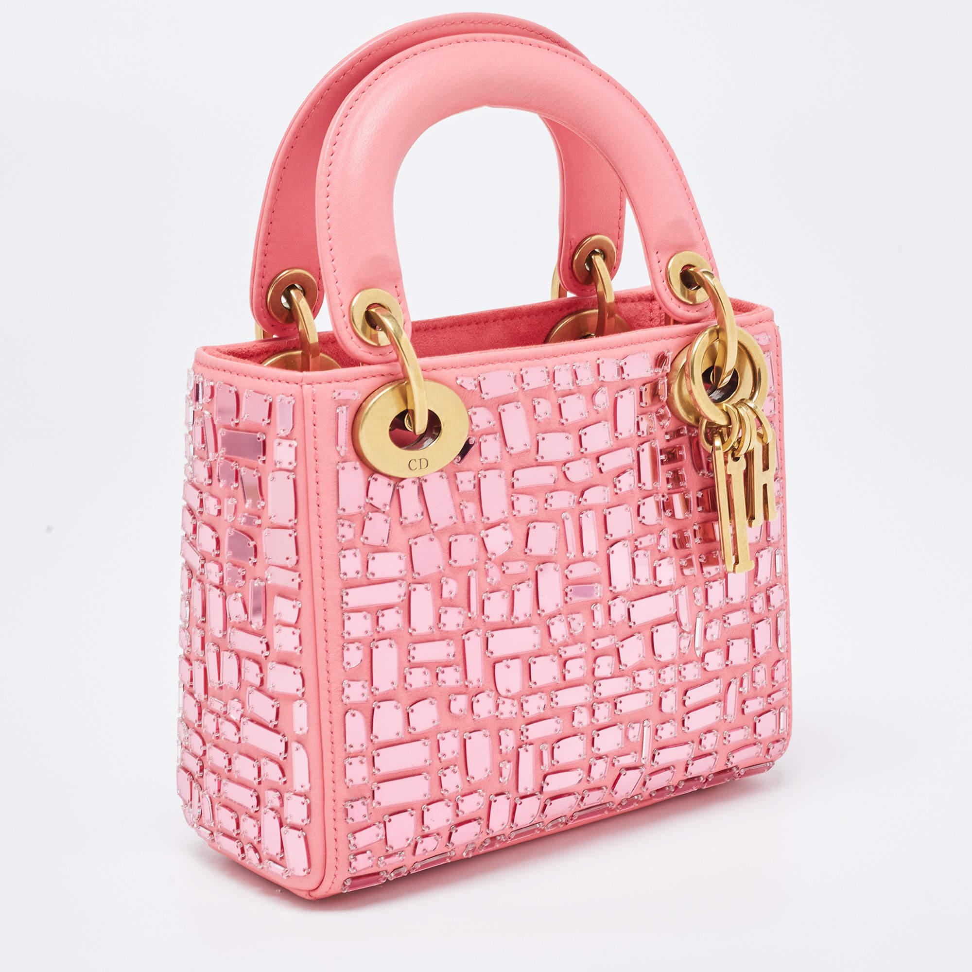 The Lady Dior tote is a luxurious and exquisite fashion accessory. Crafted from supple pink leather, it features a stunning mosaic of mirrored pieces that create a captivating visual effect. The mini size makes it perfect for on-the-go glamour,