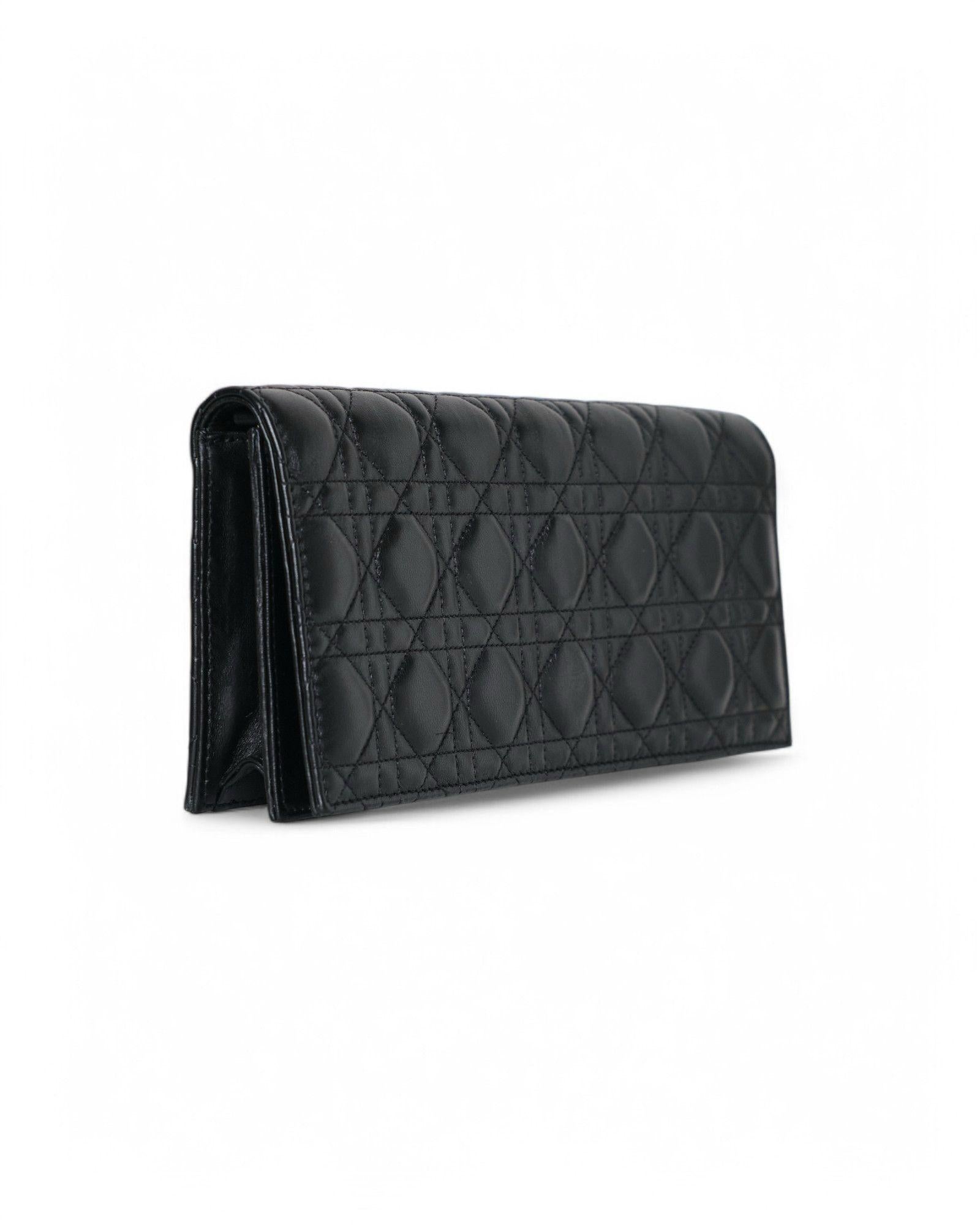 Dior signature clutch bag made of black cannage leather with gold hardware. The model features a front flap with a magnetic button closure and a tone-on-tone canvas-lined interior with a small pocket. The clutch bag is roomy enough to hold the