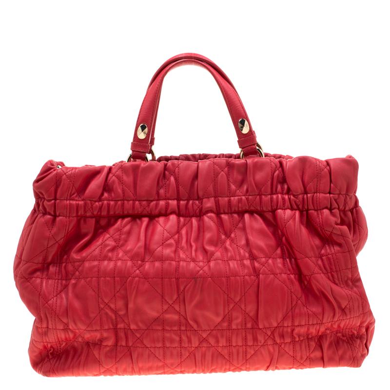 This chic bag from Dior is crafted from leather and features quilted Cannage detailing on the exterior. The red tote comes with dual handles and a leather chain strap. The buttoned closure opens to a matching leather-lined interior that has a zip