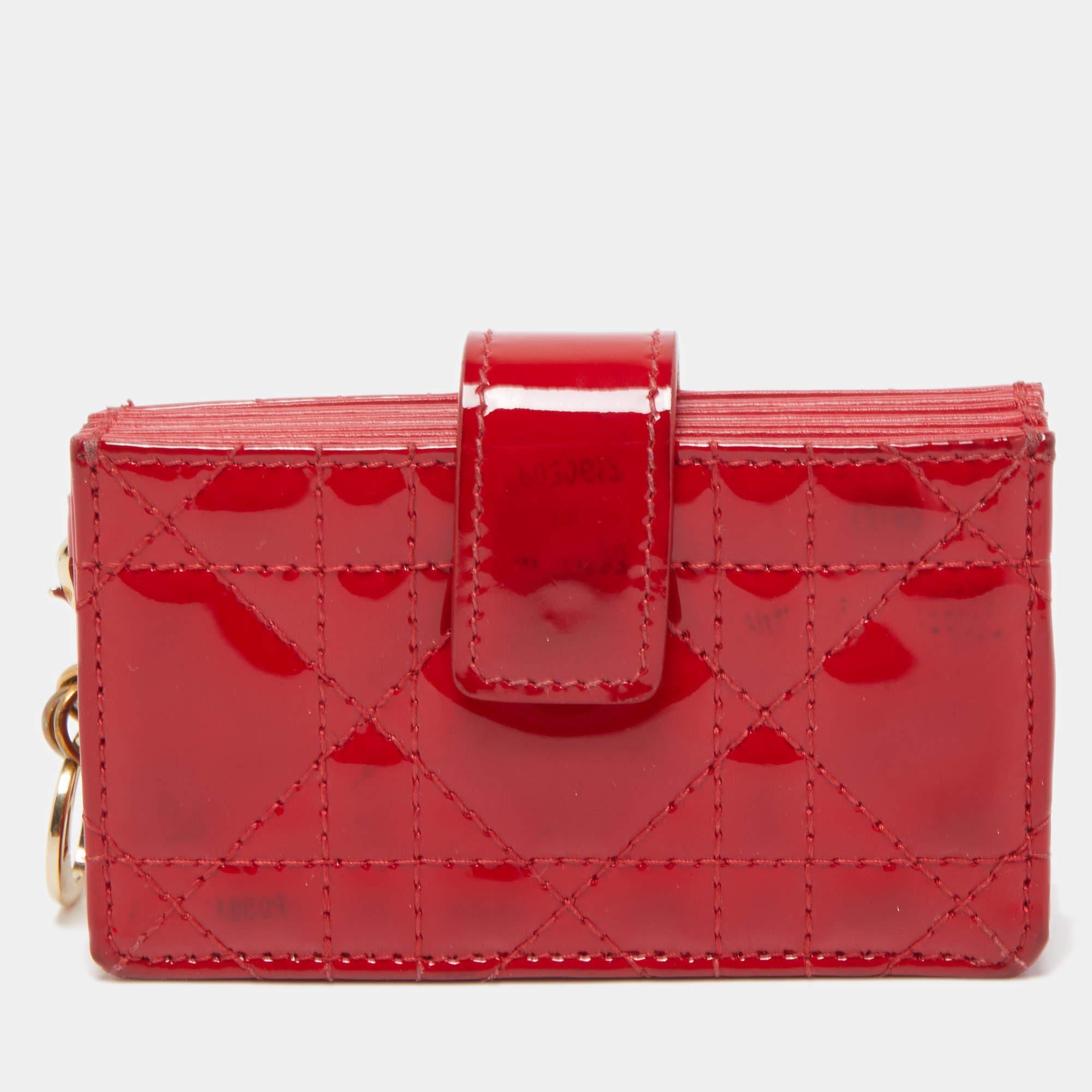 The Lady Dior gusset card case is a Dior creation that is functional, durable, and high on style! This red case has been crafted from patent leather and it carries the signature Cannage quilt. It features a front cross-over flap and opens to a nylon