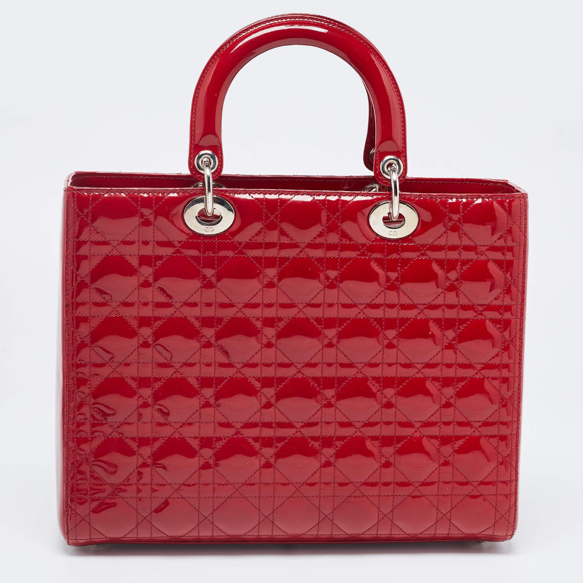 A timeless status and great design mark the Lady Dior tote. It is an iconic bag that people continue to invest in to this day. We have here this large Lady Dior tote crafted from red patent leather. The bag is complete with two top handles, a