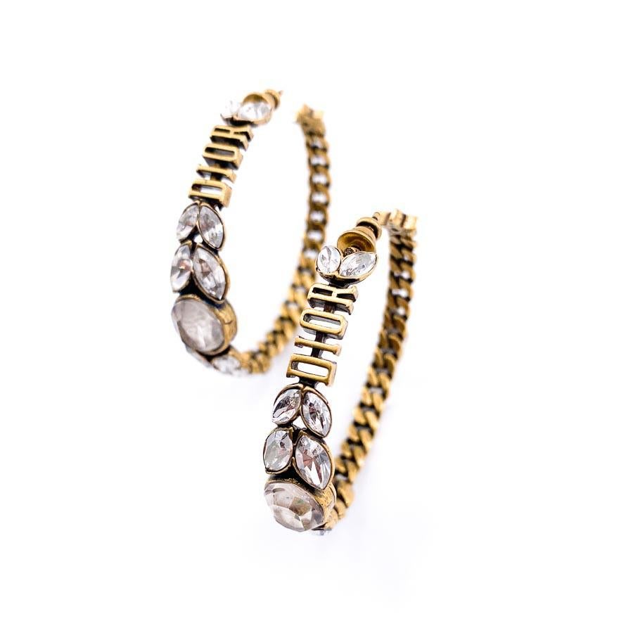 Never worn. Sold Out, aged gold and rhinestones hoop earrings from Cristian Dior. Diameter 4.5 cm. The loop is composed of a chain, the Dior name, rhinestones and its finished with a star. It's sold in its original pouch. 