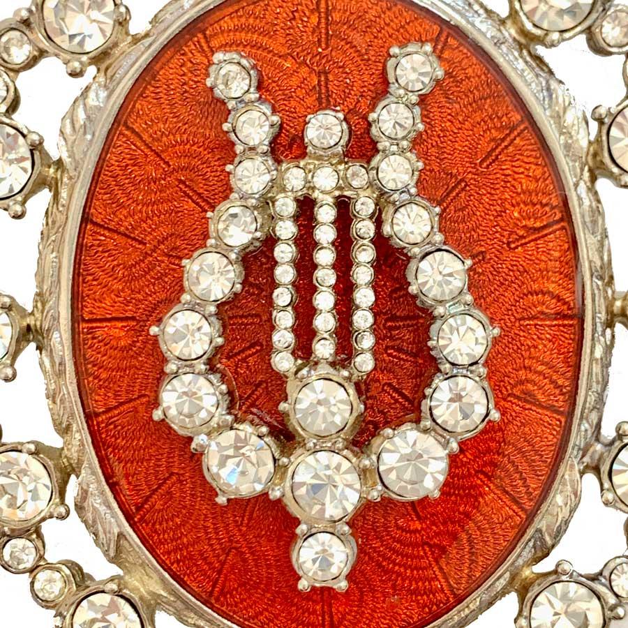 Imposing and splendid brooch of the Maison CHRISTIAN DIOR boutique, representing a lyre all in rhinestones affixed on an orange resin. All the outline is silver metal set with white rhinestones of different sizes.
The brooch also has a hook on the