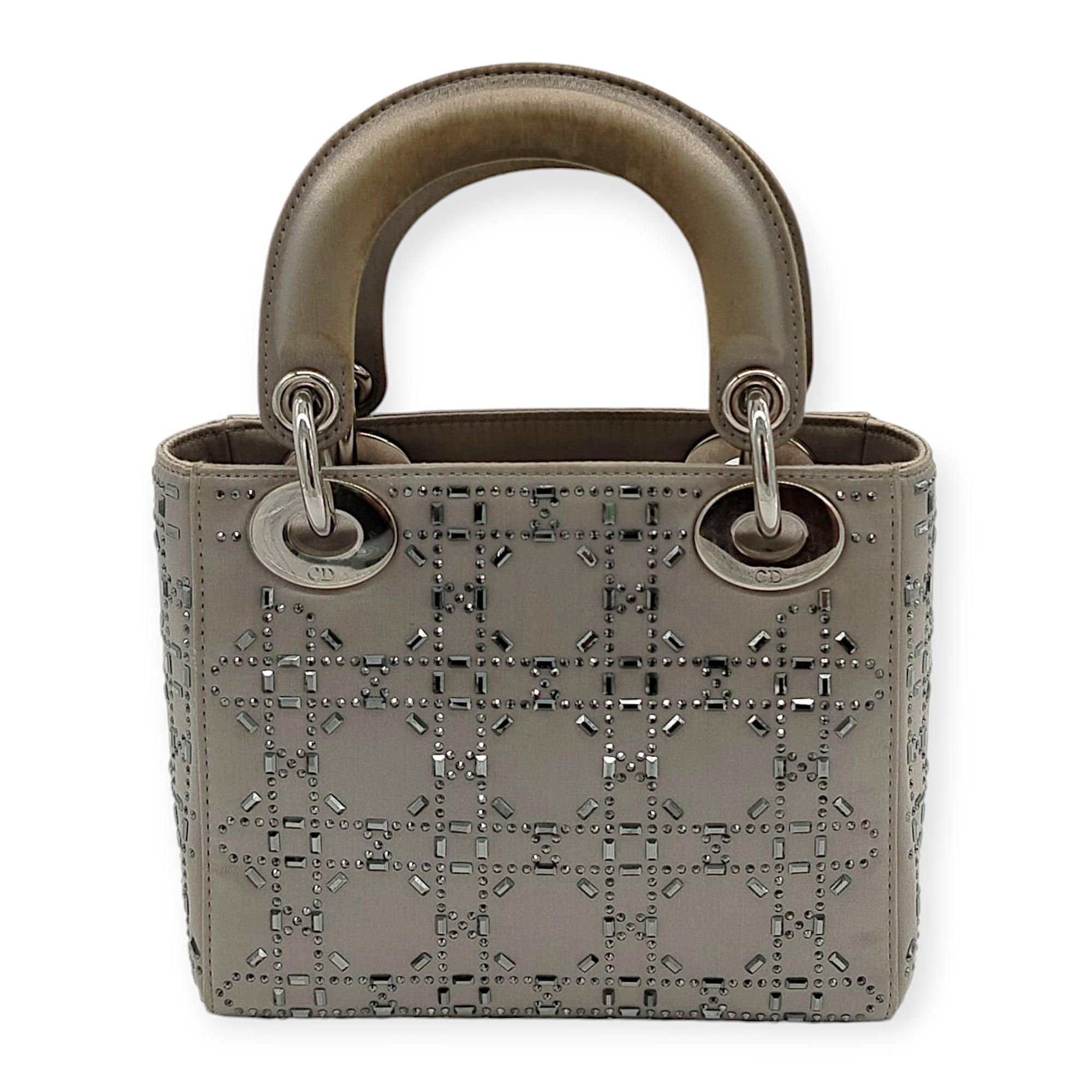 The Dior Lady Dior bag features a stunning three-compartment design in gray satin, adorned with shimmering rhinestones for an elegant touch. Complementing its luxurious look, the bag is finished with silver-tone hardware, adding a sleek and modern