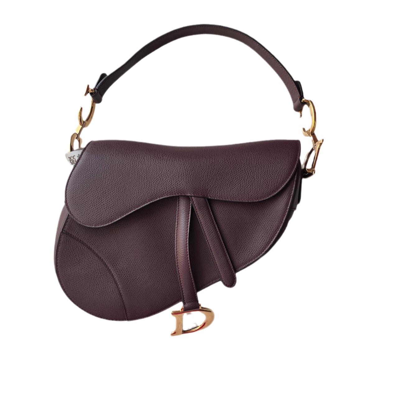 2018 Dior Saddle bag, crafted in maroon grained calfskin leather, the legendary design comes in size medium, features a magnetic flap, and antique gold-finish CD signature on both sides of the strap. 

The grained calfskin leather is extremely