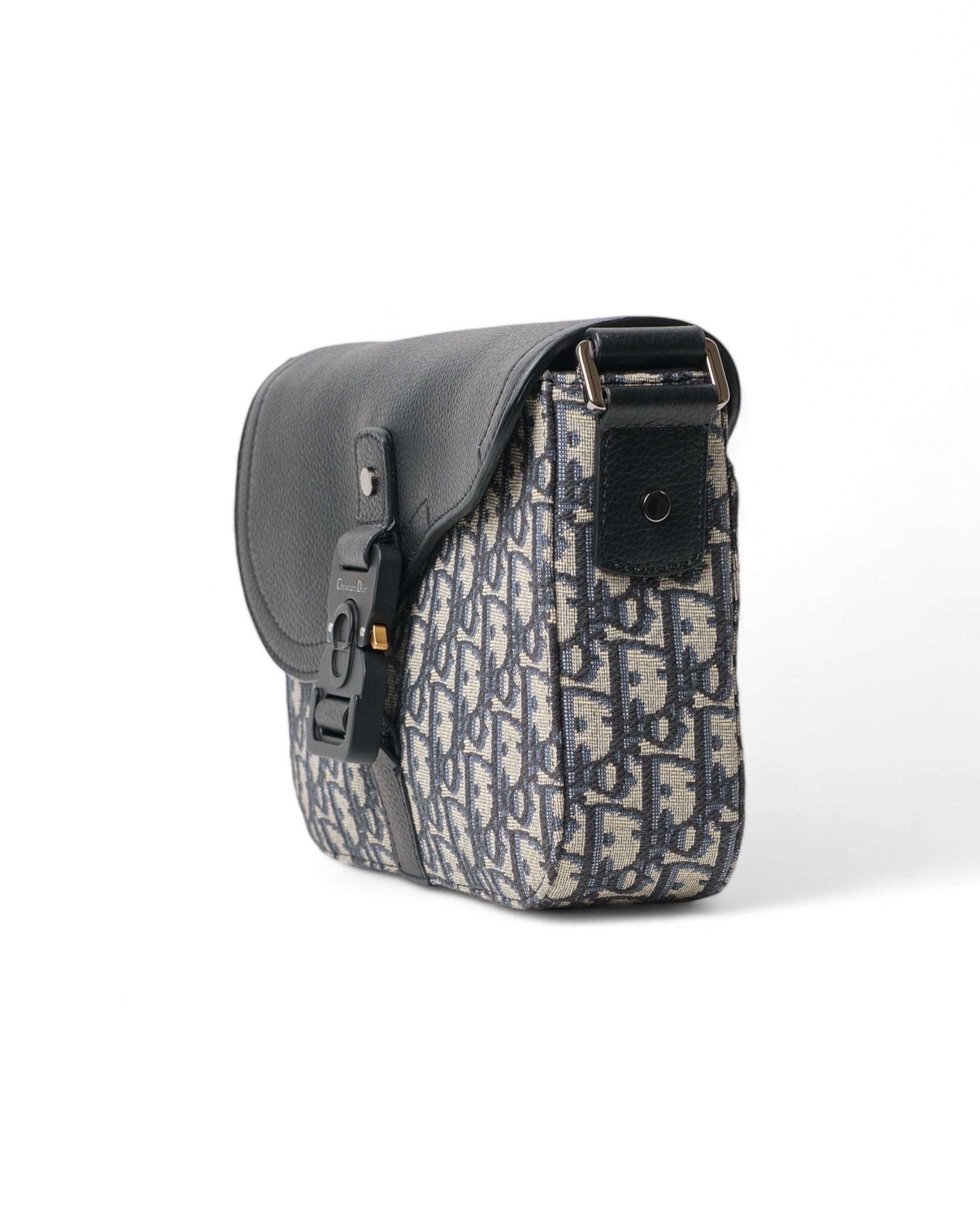 Borsa firmata Christian Dior, modello Saddle Flap, realizzata in tela Beige nella classica fantasia  Jacquard Oblique e hardware argentati, dotata di una patta frontale con chiusura ad incastro. Internamente rivestita in tela tono su tono con tasca,