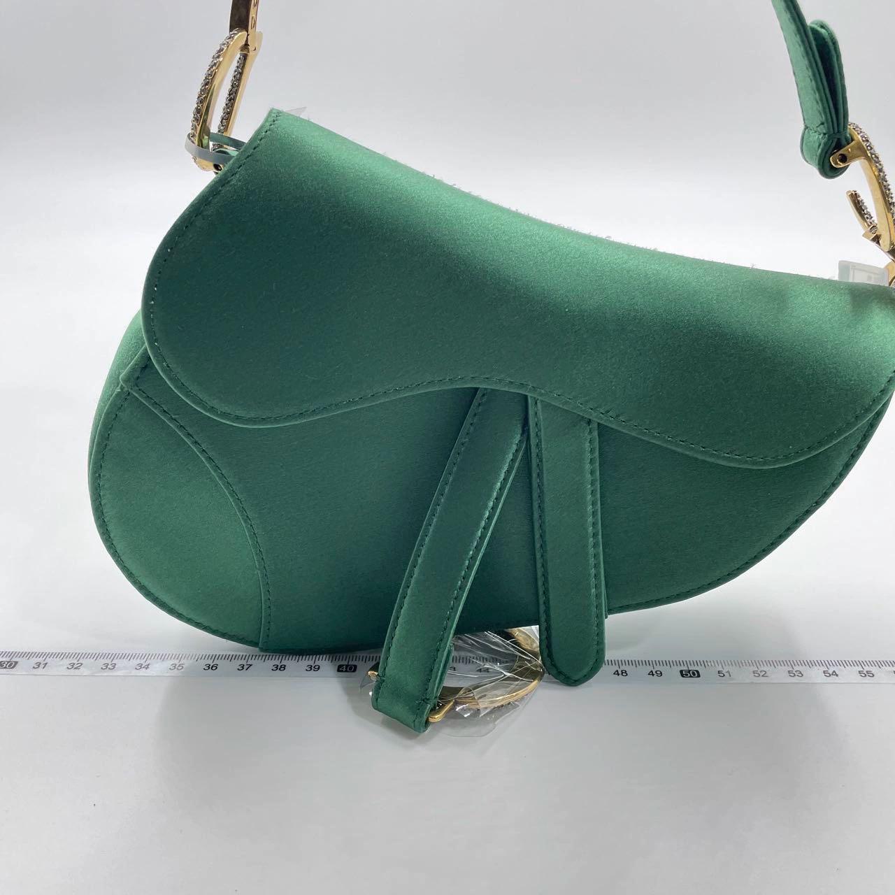 Dior Saddle bag, crafted in Emerald Green silk satin, the legendary design comes in size mini, features a magnetic flap, and bedazzling crystal embellished CD signature on both sides of the strap. The Saddle bag may be carried by hand. 

The silk