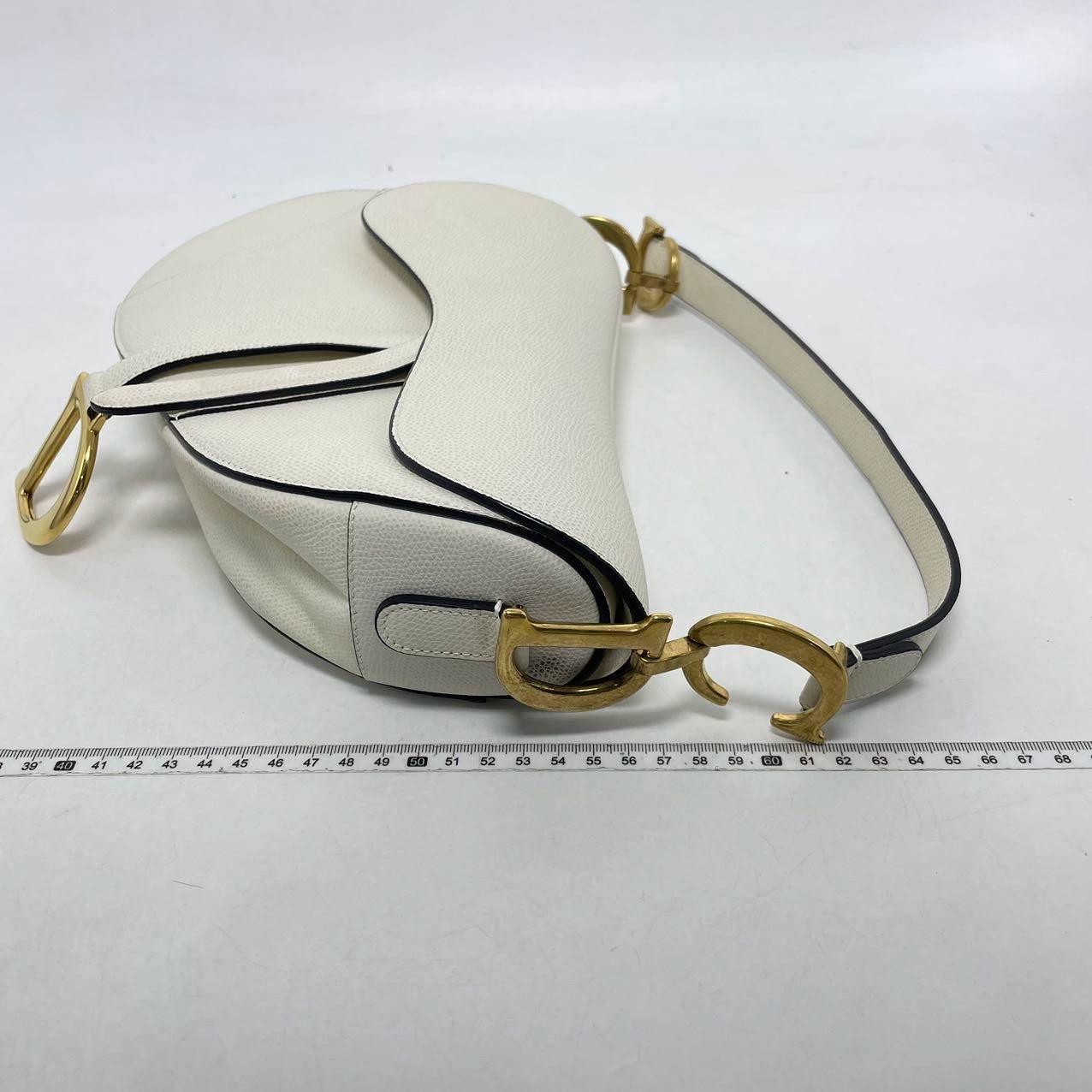 2018 Sac Saddle Dior, réalisé en cuir de veau grainé blanc, le modèle légendaire est proposé en taille moyenne, présente un rabat magnétique et la signature CD en finition or antique de part et d'autre de la lanière. La sacoche peut être portée à la