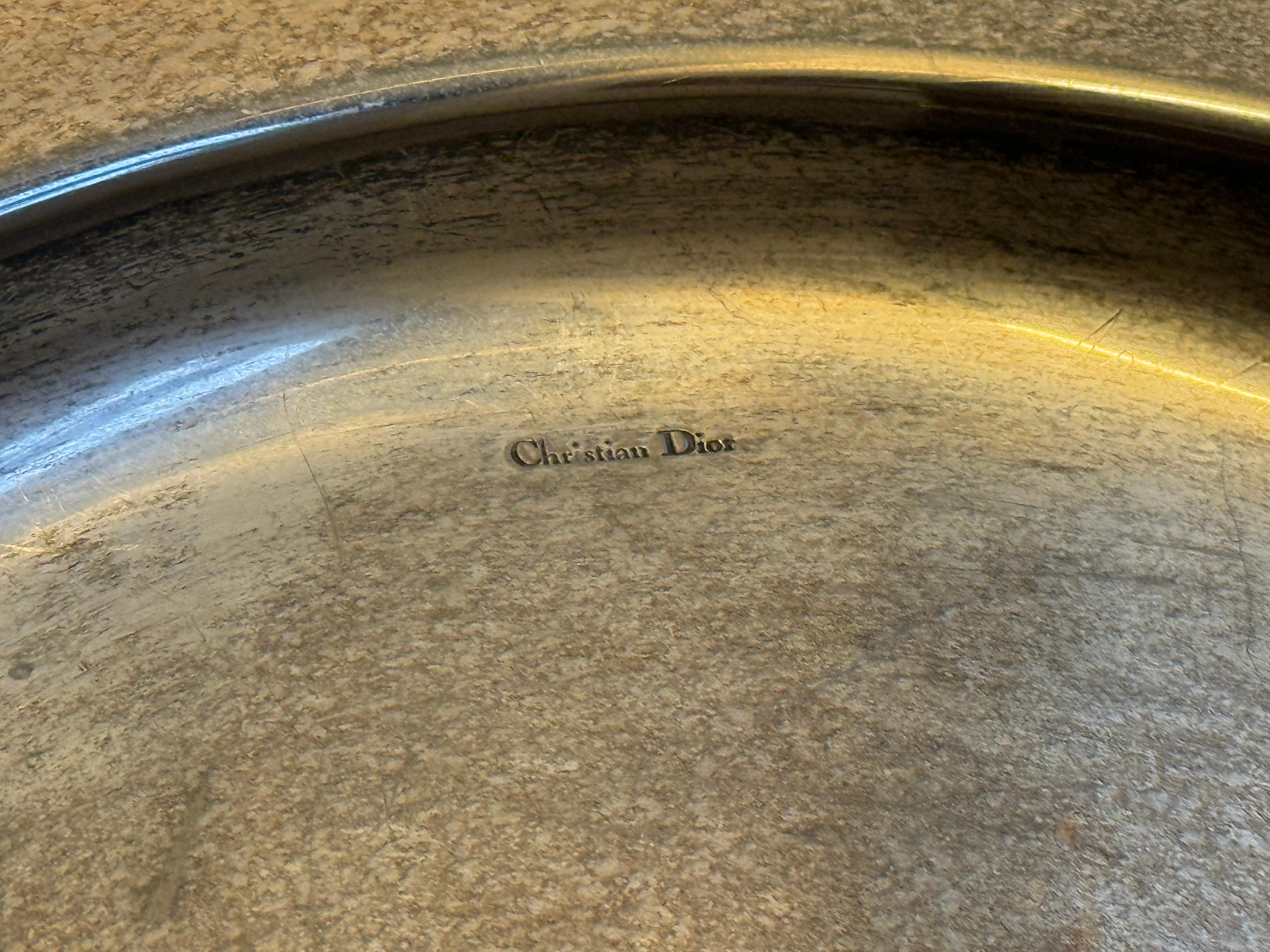 Ce plateau vintage Dior en métal argenté est un exemple élégant de la sensibilité raffinée de la Maison en matière de design. Fabriqué en argent poli, le plateau est encadré d'un motif de chaîne tressée qui ajoute à la fois texture et dimension,