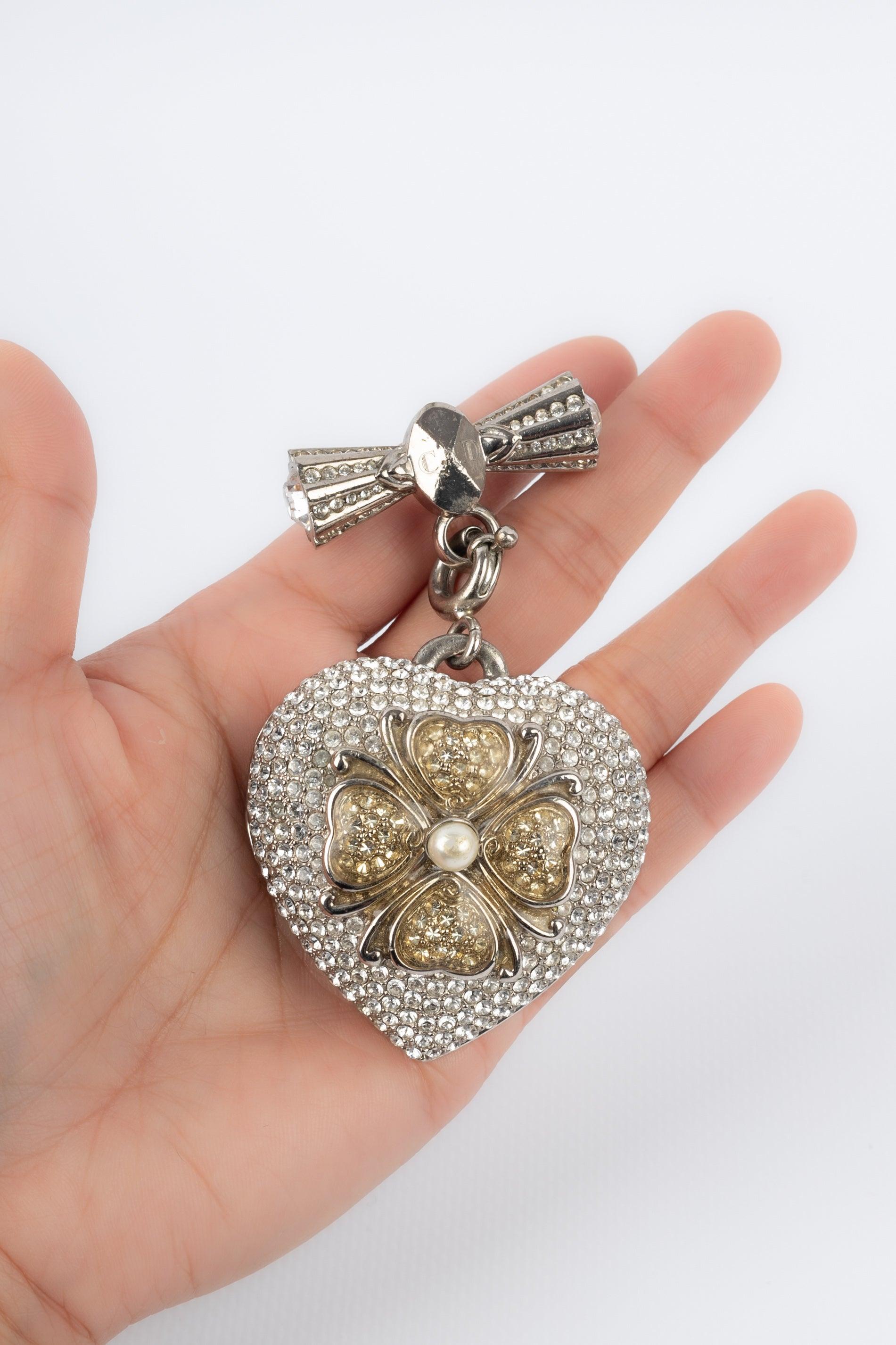 Dior- Broche en métal argenté avec strass représentant un cœur surmonté d'un trèfle à quatre feuilles. Le pendentif contient un miroir. A signaler, quelques rayures sur le métal.

Informations complémentaires :
Condit : Bon état
Dimensions : 8,5 cm